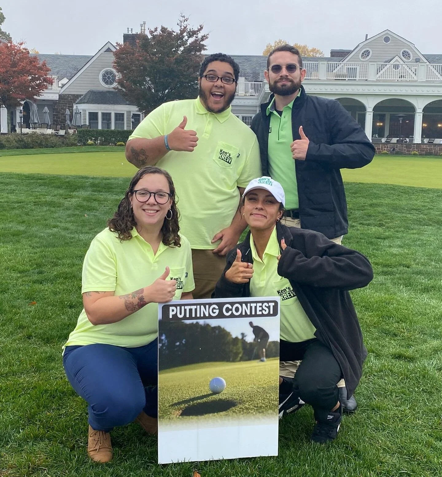 Four people stand on a golf course next to a sign for a putting contest, a classic golf tournament fundraiser ideas.