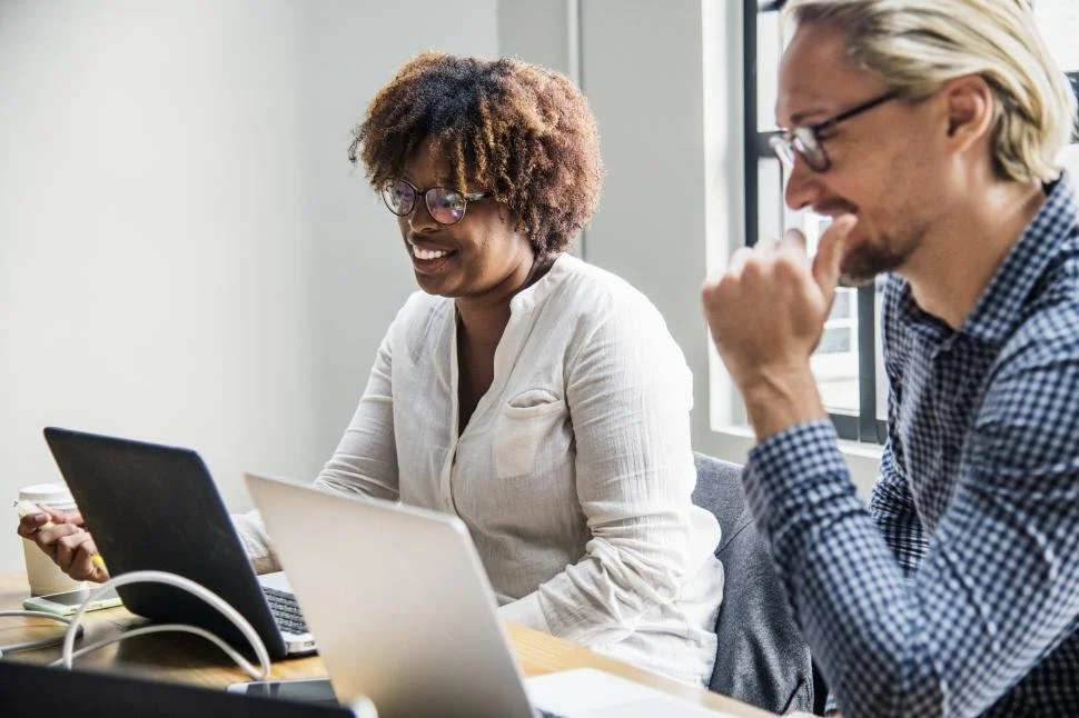 Two people work on computers at a table.