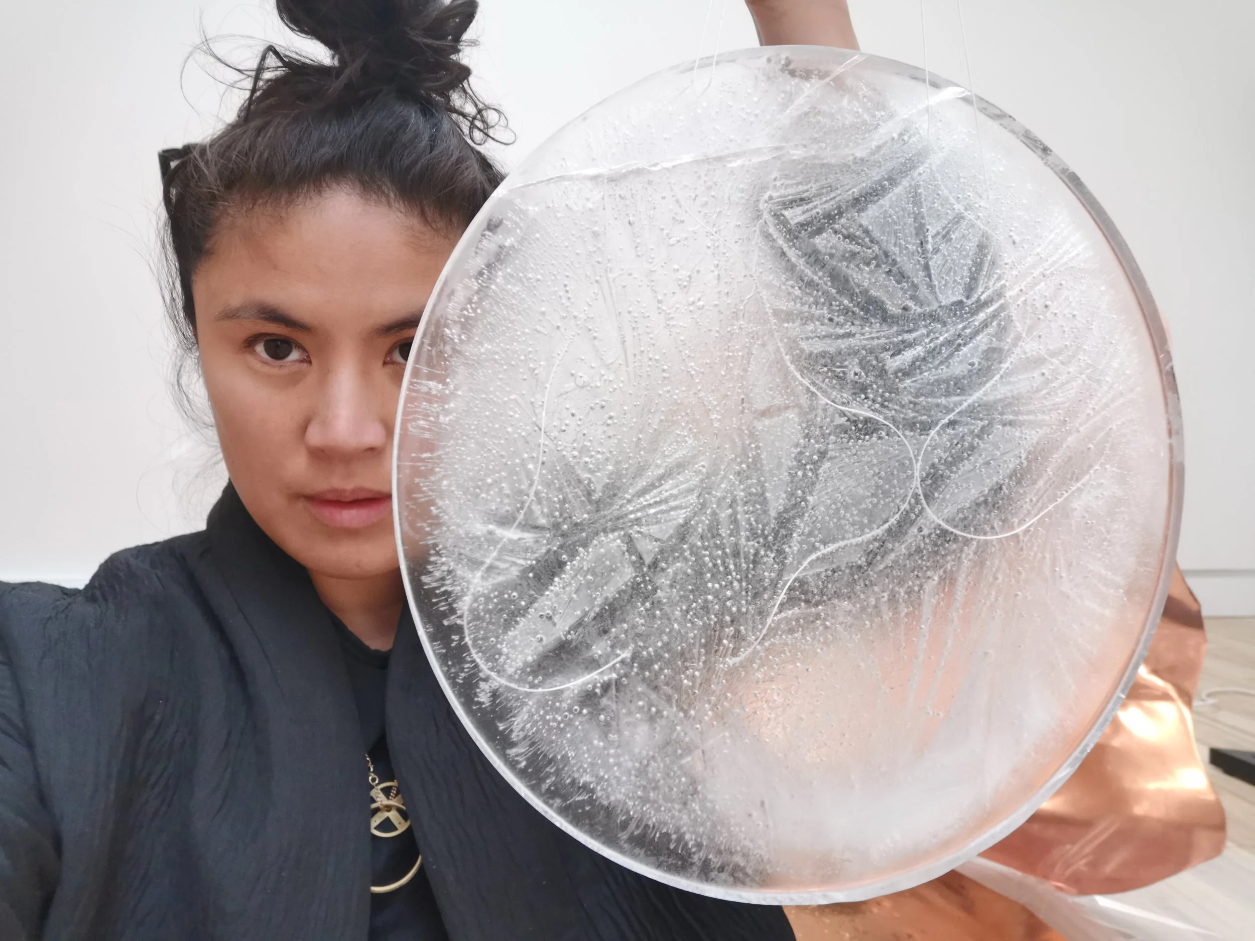 April Aliermo faces the camera while holding a flat round disc of ice in front of her face