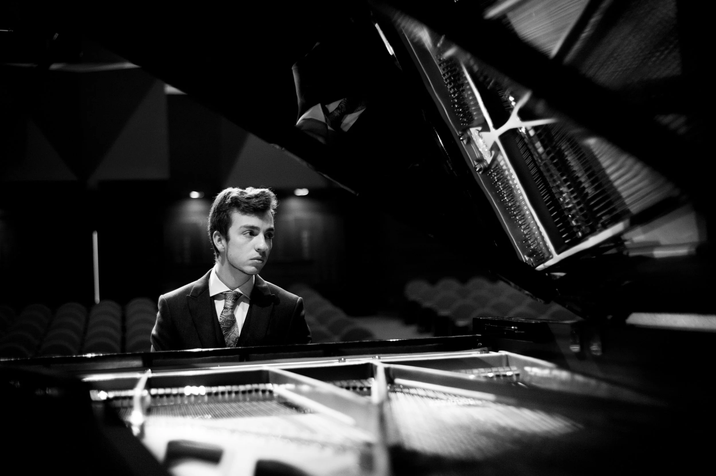 Stephen Eckert, a pianist, is at a grand piano in a concert hall wearing a suit and tie. The image is dramatic and in black and white.