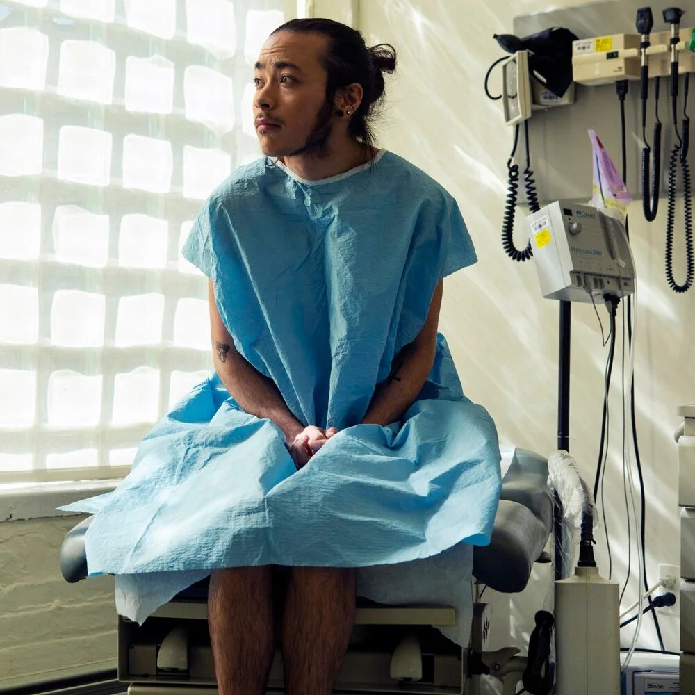 A%2Bgenderqueer%2Bperson%2Bsitting%2Bin%2Ba%2Bhospital%2Bgown%2Bsitting%2Bin%2Ban%2Bexam%2Broom.jpg
