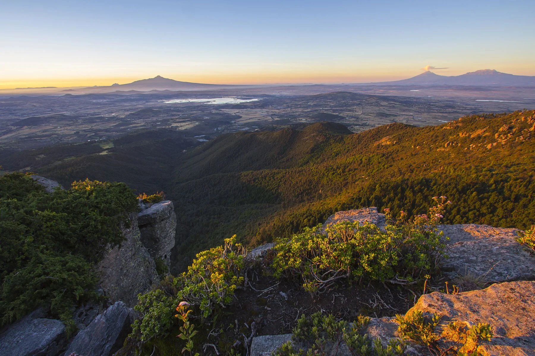 En mi primer plano se aprecia los cerros cubiertos de bosque, posteriormente esta la presa de Atlangatepec y al fondo se logran apreciar Popocatépetl, Iztaccíhuatl, y Malintzi