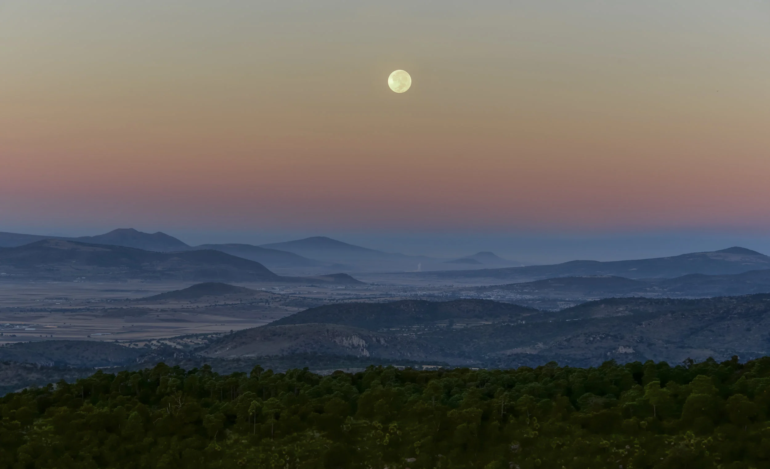 Valle de puebla cubierto de neblina, con un cielo de tonos rosados y luna llena