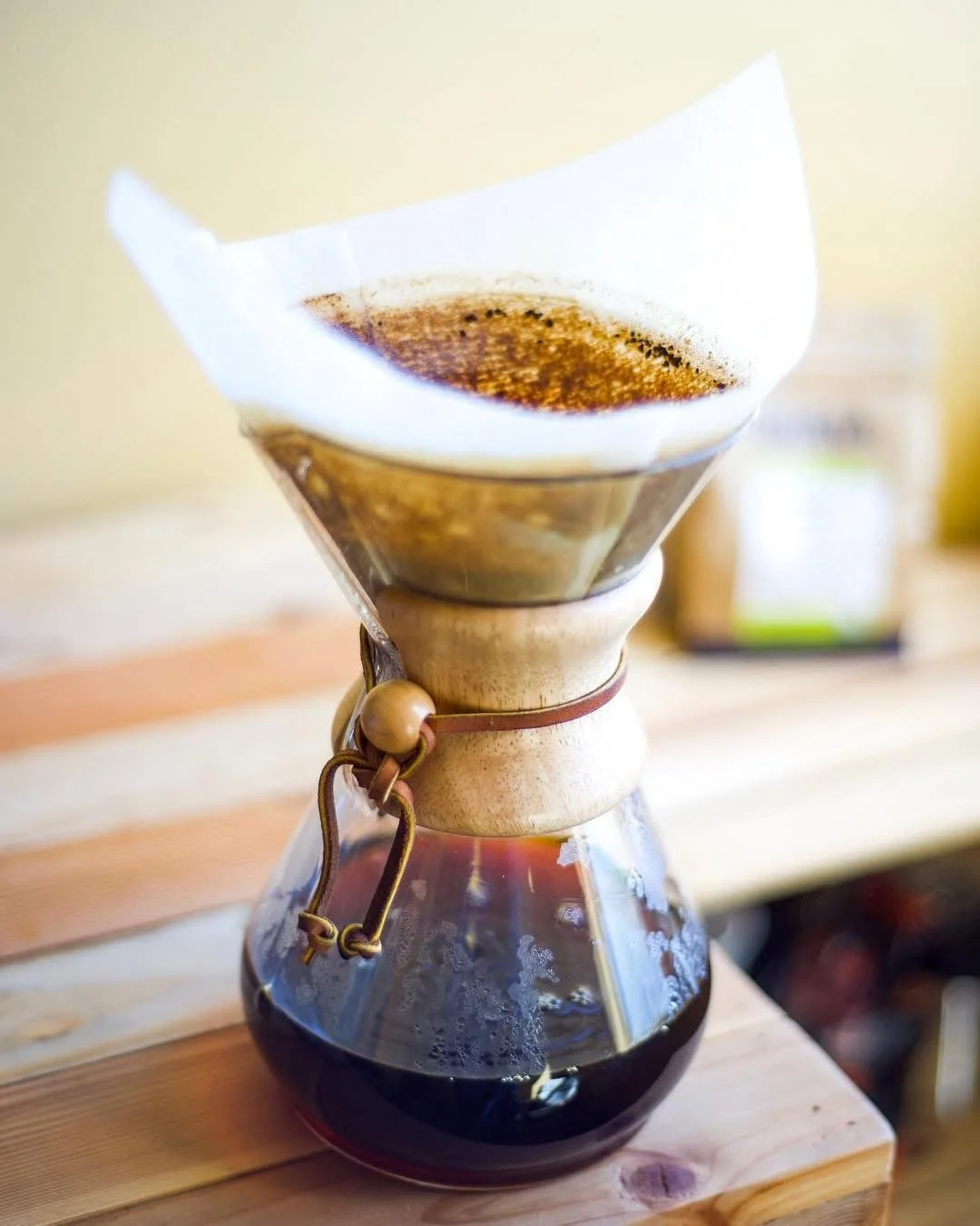 Pour-over coffee maker with dark brewed coffee, situated on a wooden surface.