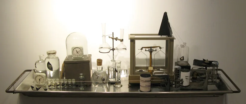 Body of Evidence: Testing the Possibility of Escape by Sea, Vintage glass, weather recording devices, clocks, scales, metronome, metal boxes, weights, water, paper, beeswax, and string, on a morgue body tray. (Kinetic sculpture with slowly moving boats and graphs.) 78 x 26 x 23 inches, 2013.