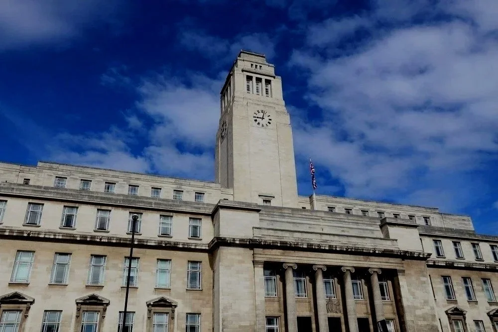 A large historic building with a prominent clock tower against a blue sky with clouds.