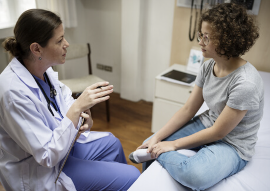 A doctor talking to a young woman sitting on an examination table in a medical office.