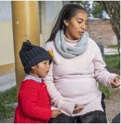 A woman and a young girl outdoors, with the woman holding a smartphone while the girl looks on.