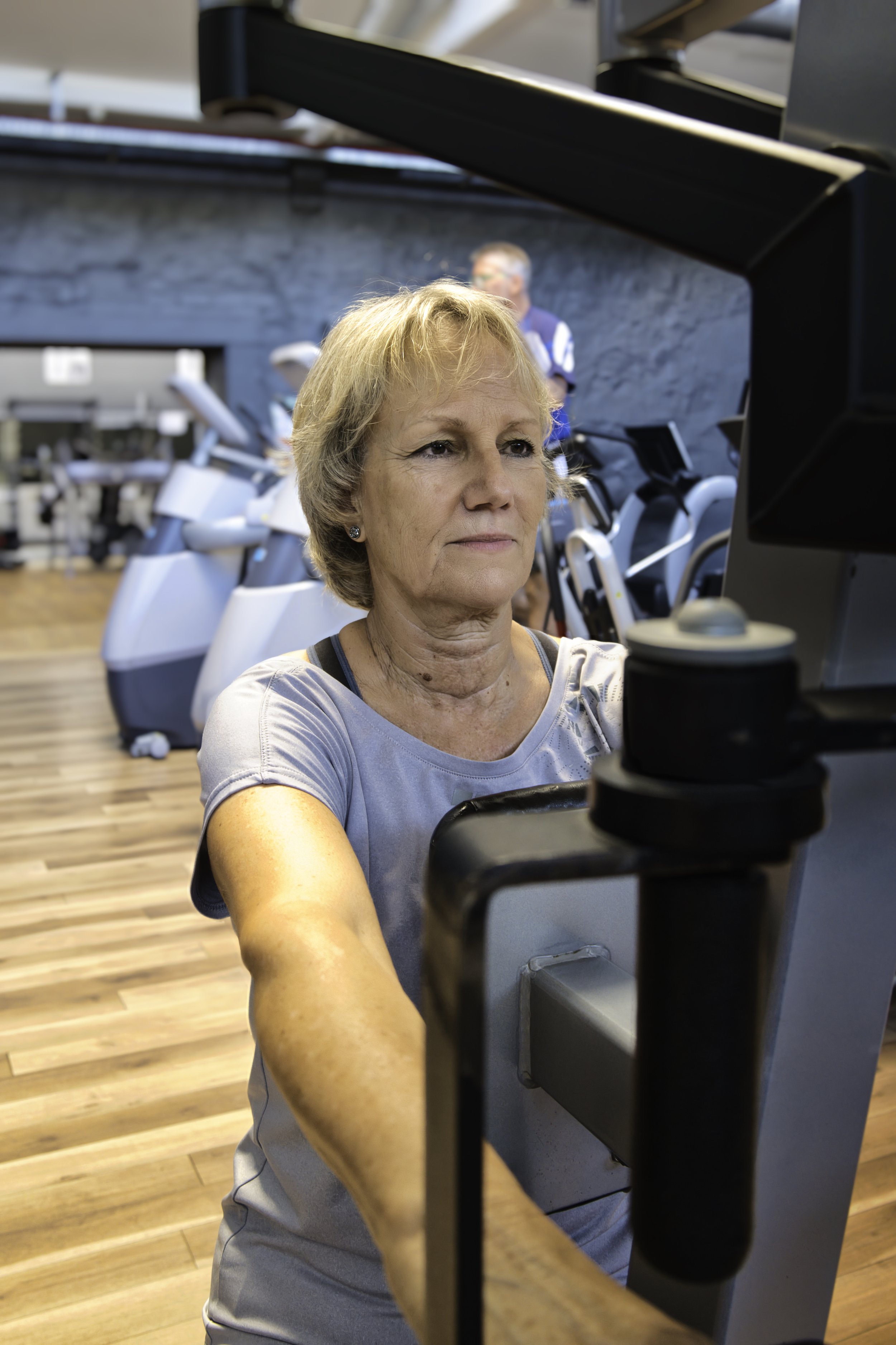 Ältere Frau beim Training auf einem Fitnessgerät in einem Fitnessstudio.