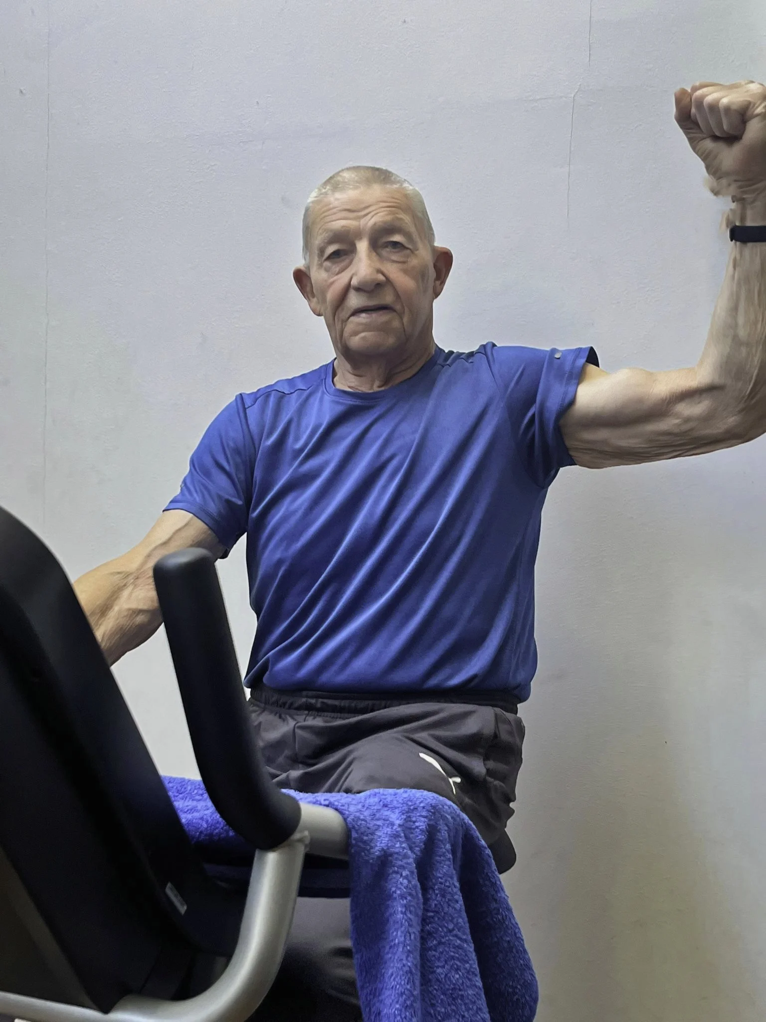 Ein alter Mann in sportlicher Kleidung, der auf einem Fitnessgerät trainiert und eine Faust in die Luft reckt.