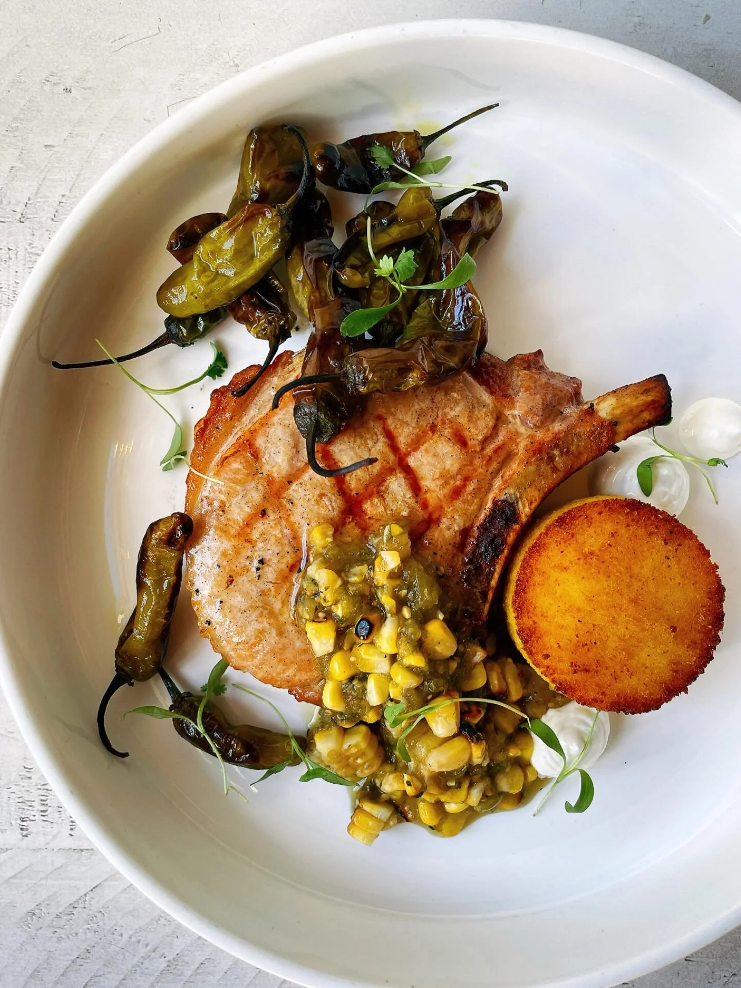 Last few days of our pork rib chop! Currently served with blistered shishitos, corn salsa verde, cheesy polenta cake, lemon crema.