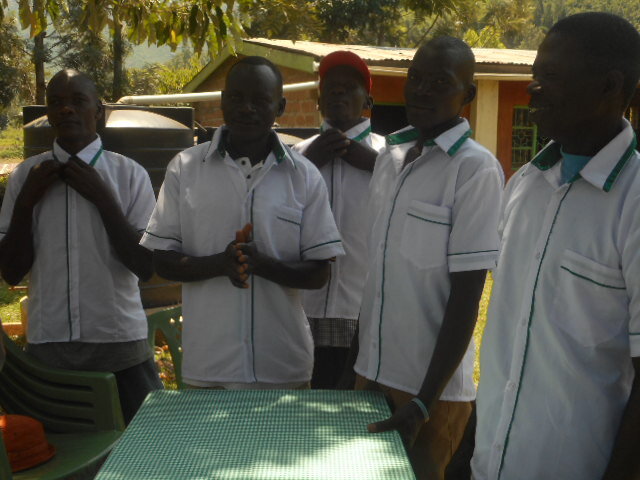  Five men dressed in white jackets and green trim are standing around a table with a white and green checked tablecloth, ready to serve a catering event in the village.