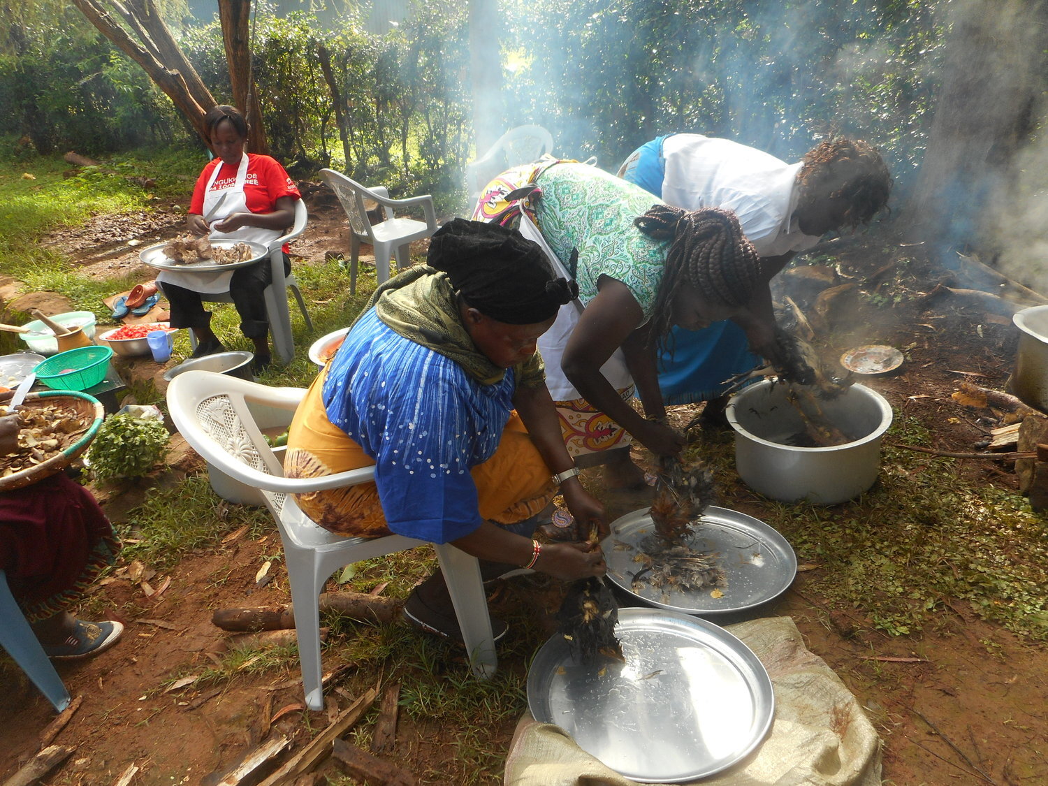 Four villagers who are in the microfinance Women’s group are preparing food with a cooking fire 