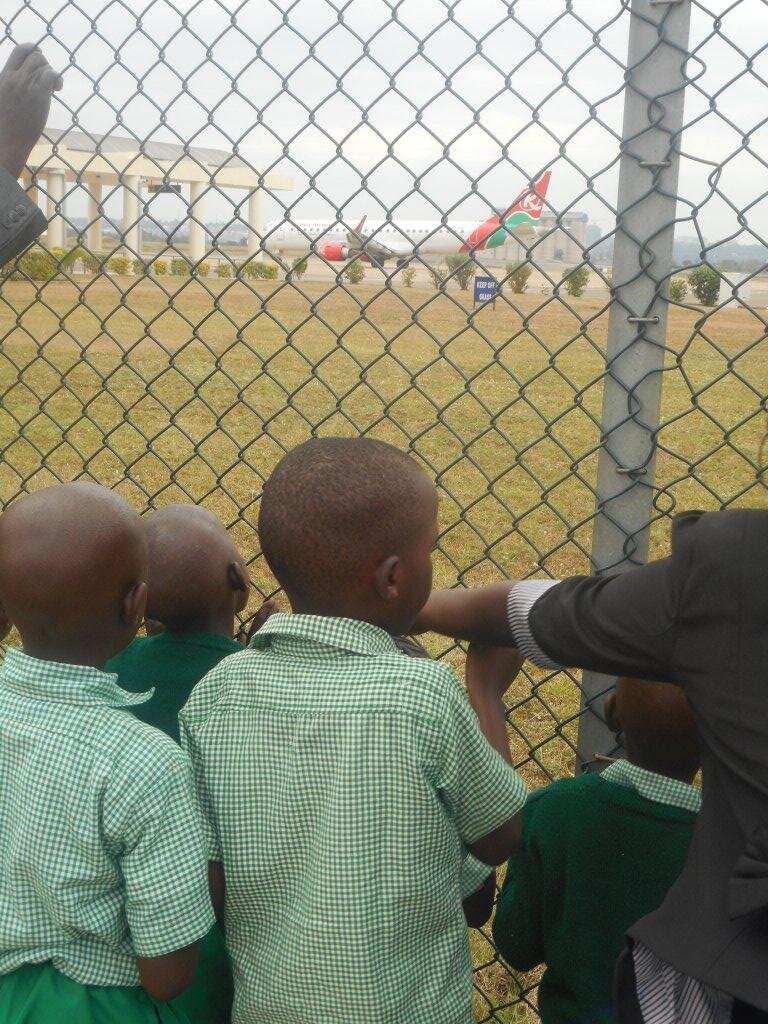 A few schoolchildren look through a fence at an airplane