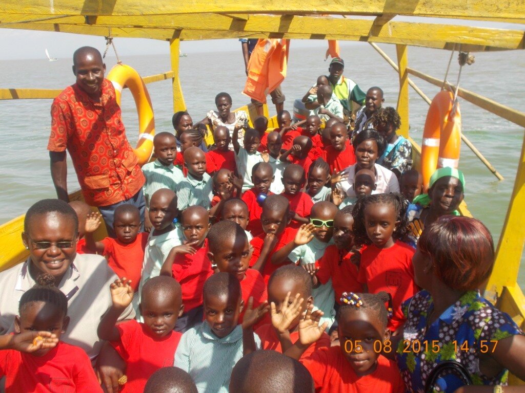 A crowd of schoolchildren in green and red uniforms sits on a boat with adults
