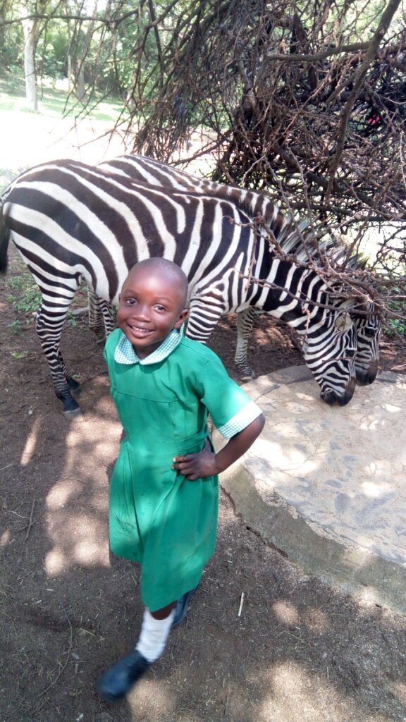 A schoolgirl smiles in front of two zebras