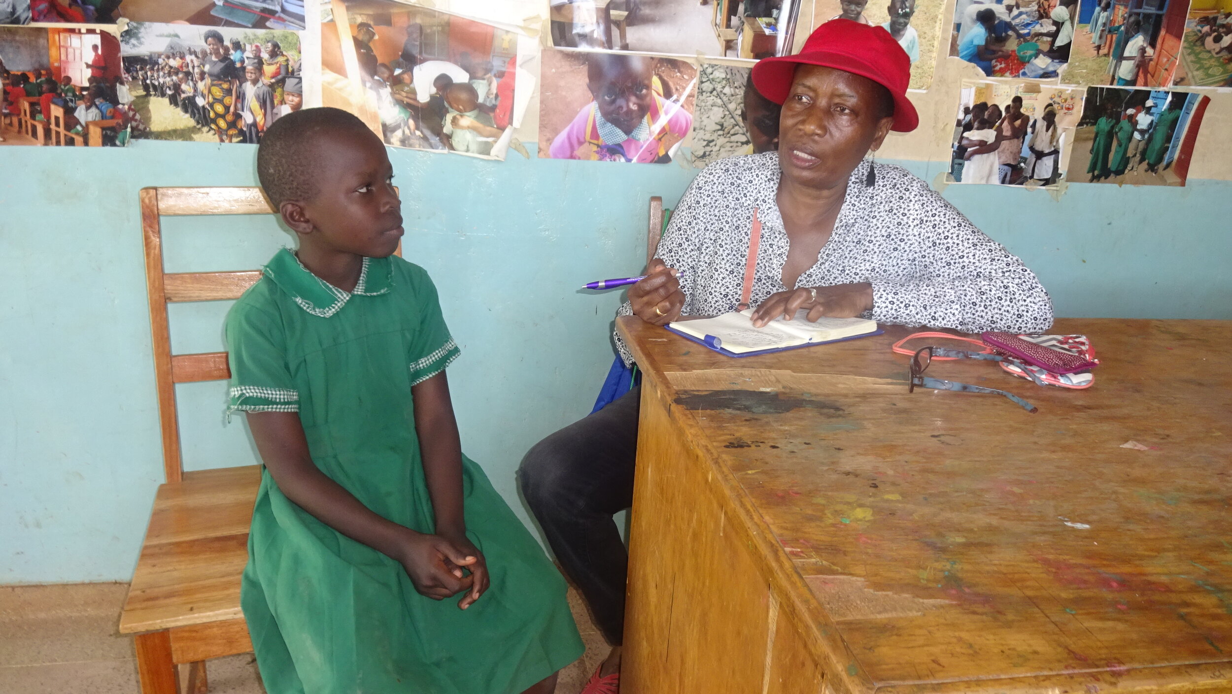 Mwanzo’s Executive Director, Loyce Ong’udi is seated at a table in a school classroom