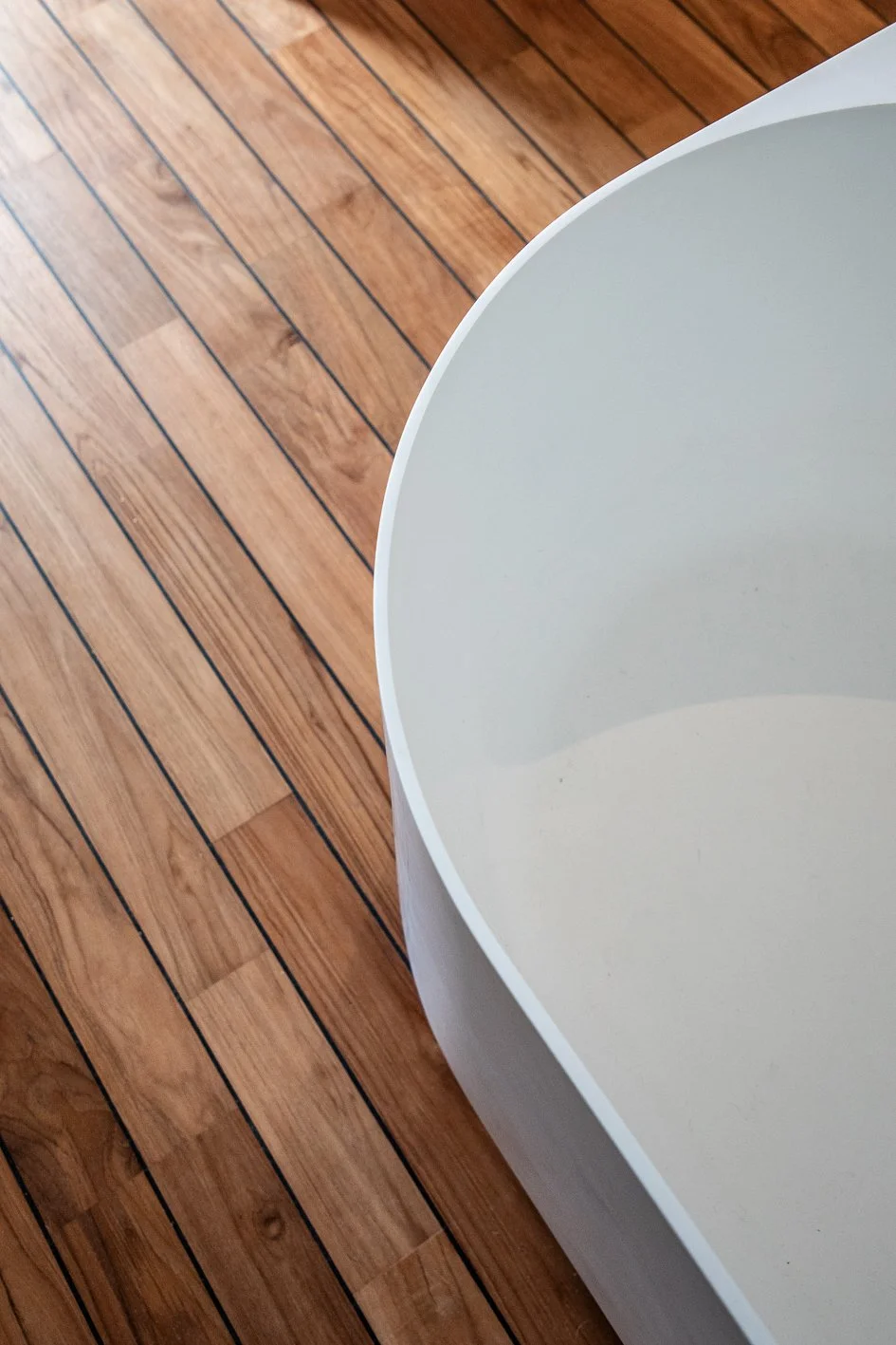 détail d'un rebord de baignoire design et d'un parquet de style pont de bateau. Photographie d'architecture intérieure prise en lumière naturelle dans le brabant wallon