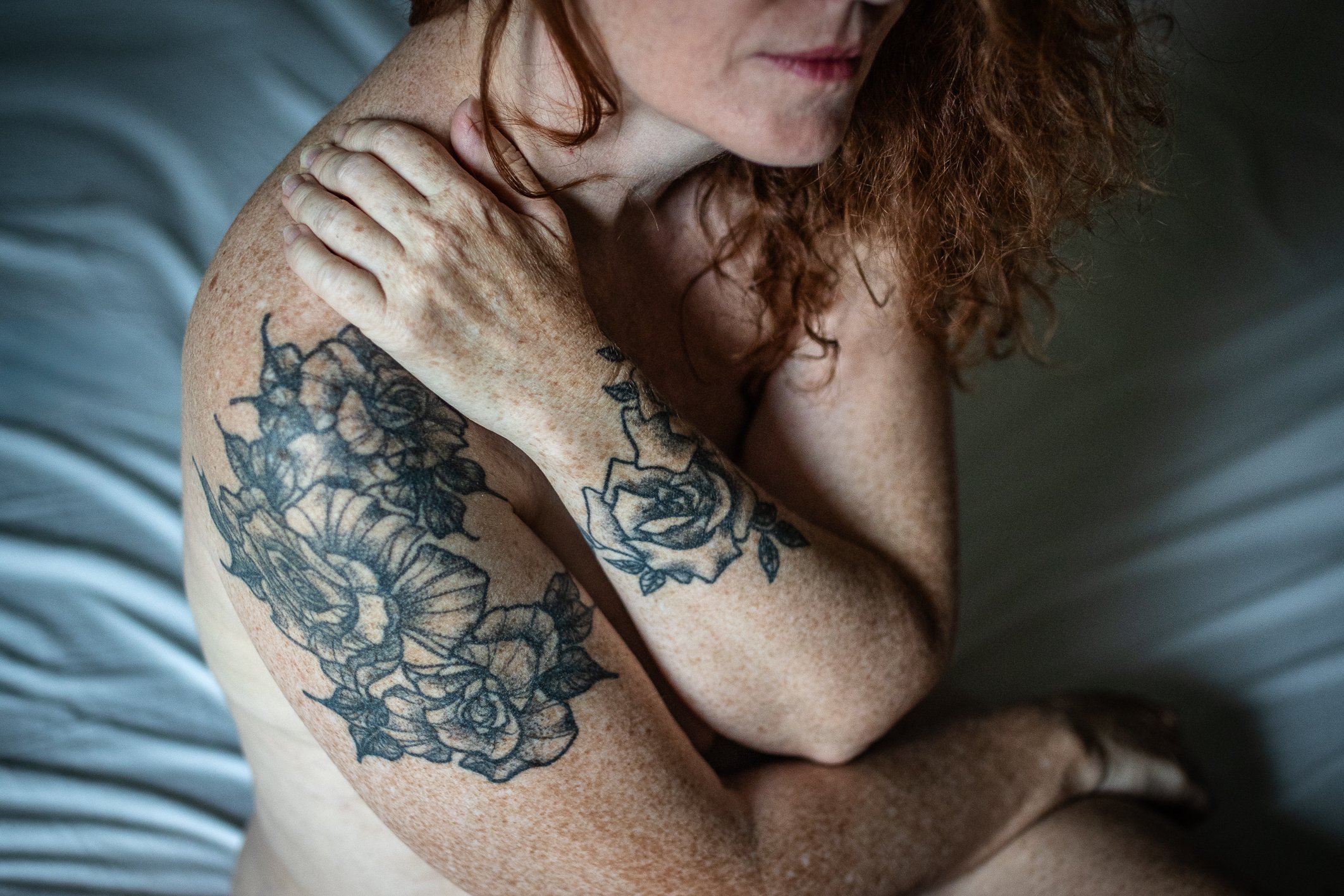 photographie de boudoir en lumière naturelle poétique. La beauté de la femme et ses tatouages au motif floral est mis en avant.