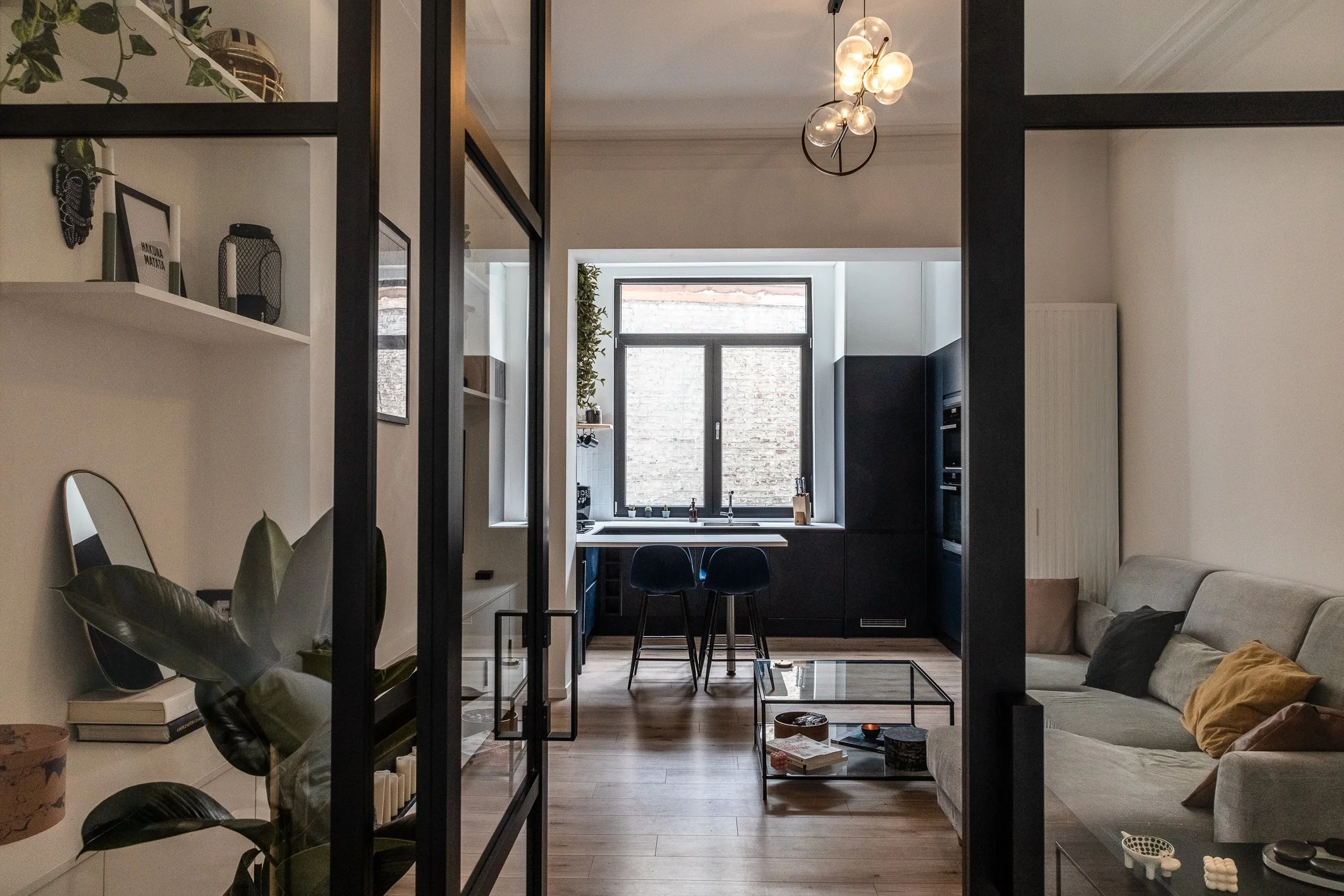 Appartement rénové à Bruxelles avec cuisine contemporaine et îlot central sur mesure, salon avec meuble  à étagères  sur mesure et verrière industrielle. Photographie prise en lumière naturelle