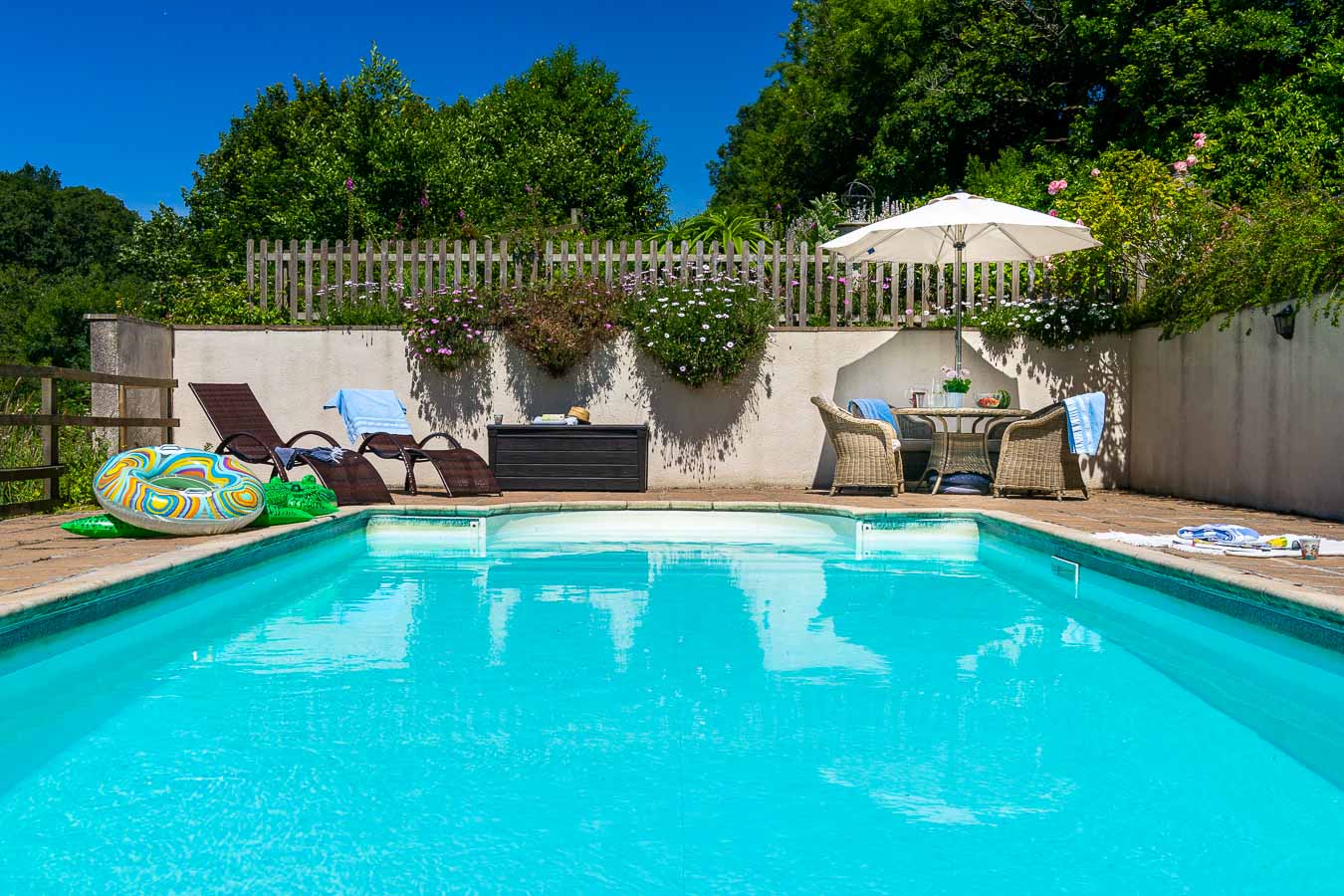 The outdoor heated swimming pool with sun loungers and rattan garden furniture with cushions and umbrella in Flear House garden.