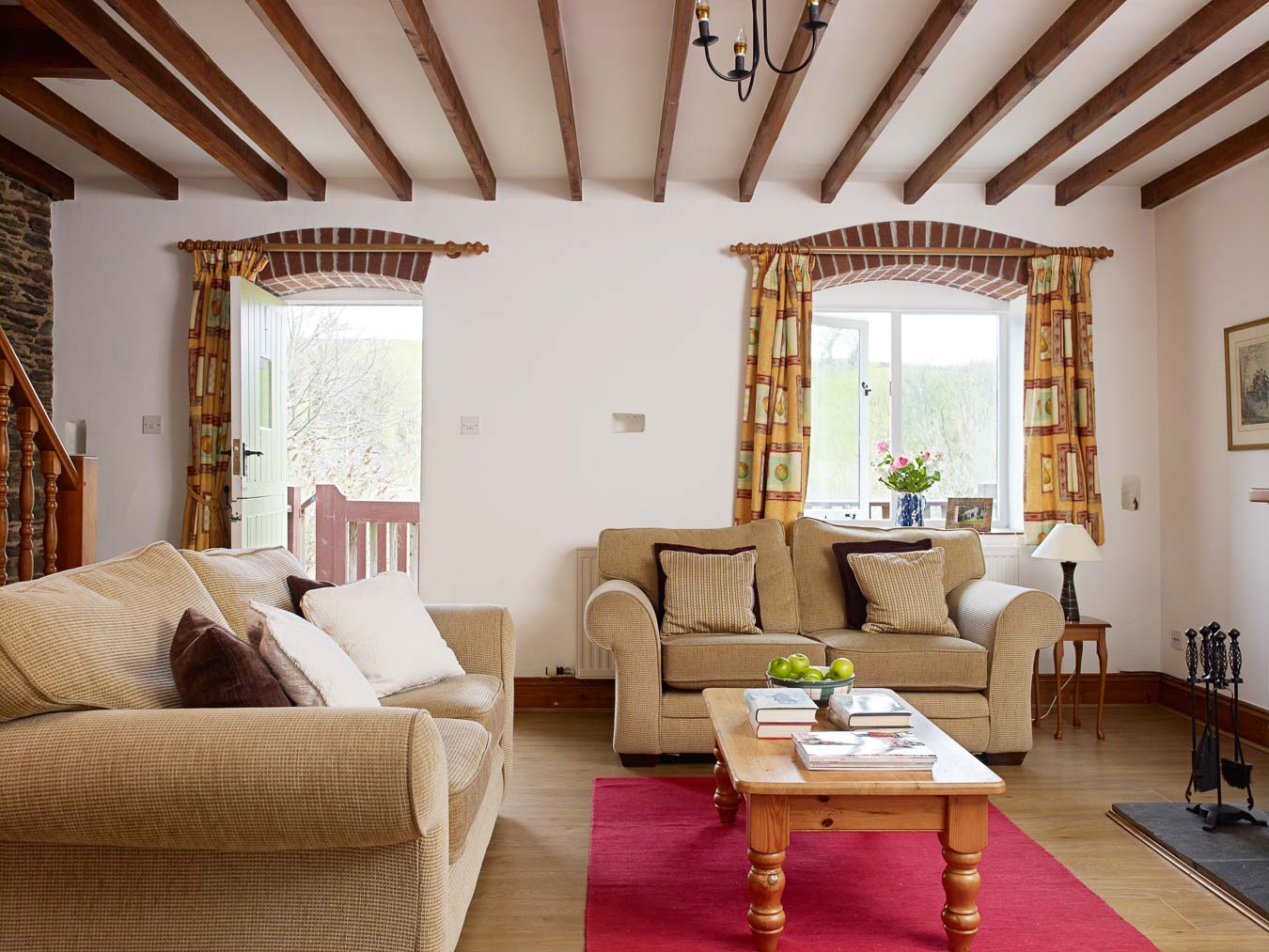 The living room at Cartwheel cottage with open fire and access onto private decking which overlooks the lawn and the Devon hills beyond at Flear Farm.