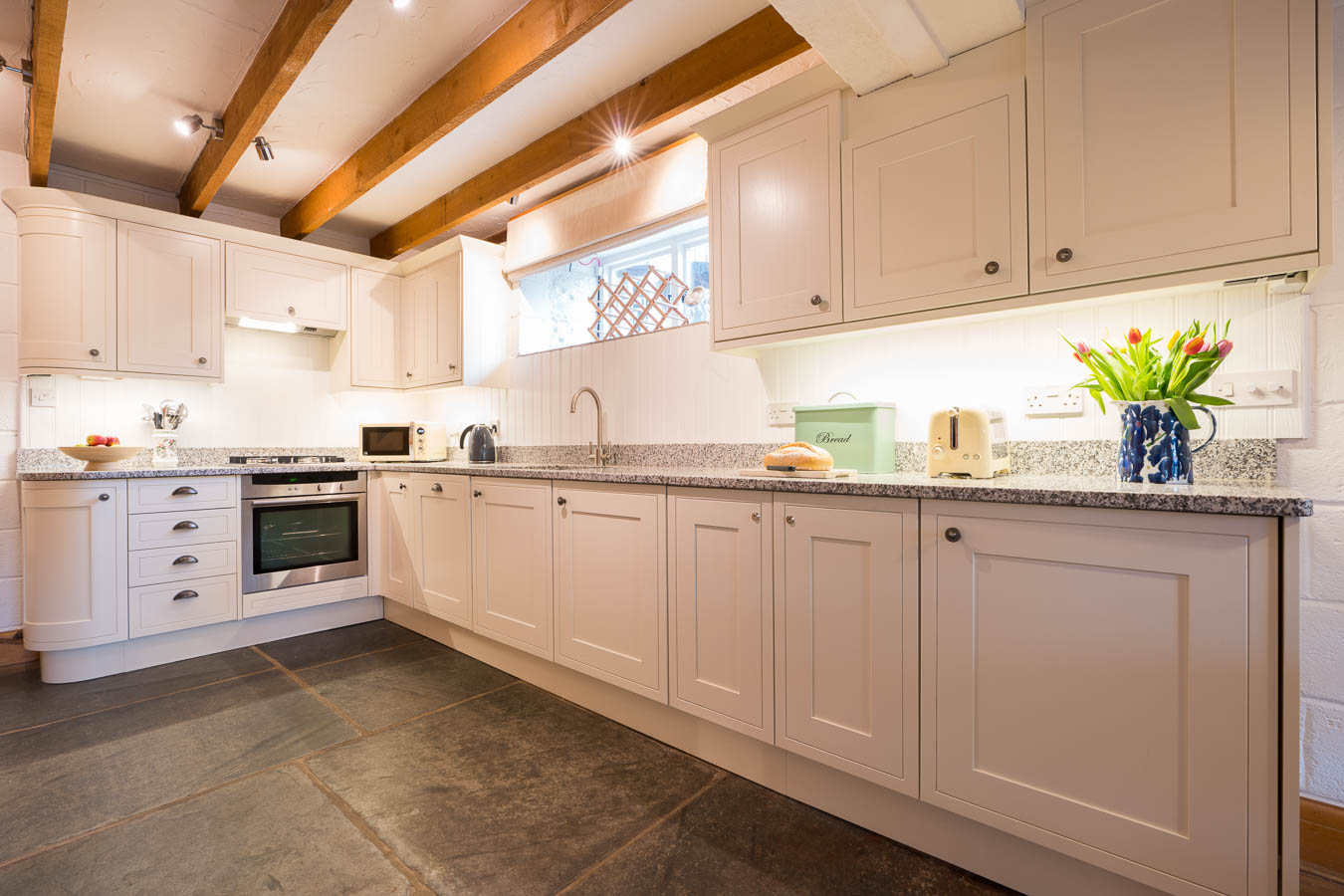 The fresh cream kitchen with granite work tops, Neff oven and original sate floors of Quarry cottage at Flear Farm. 