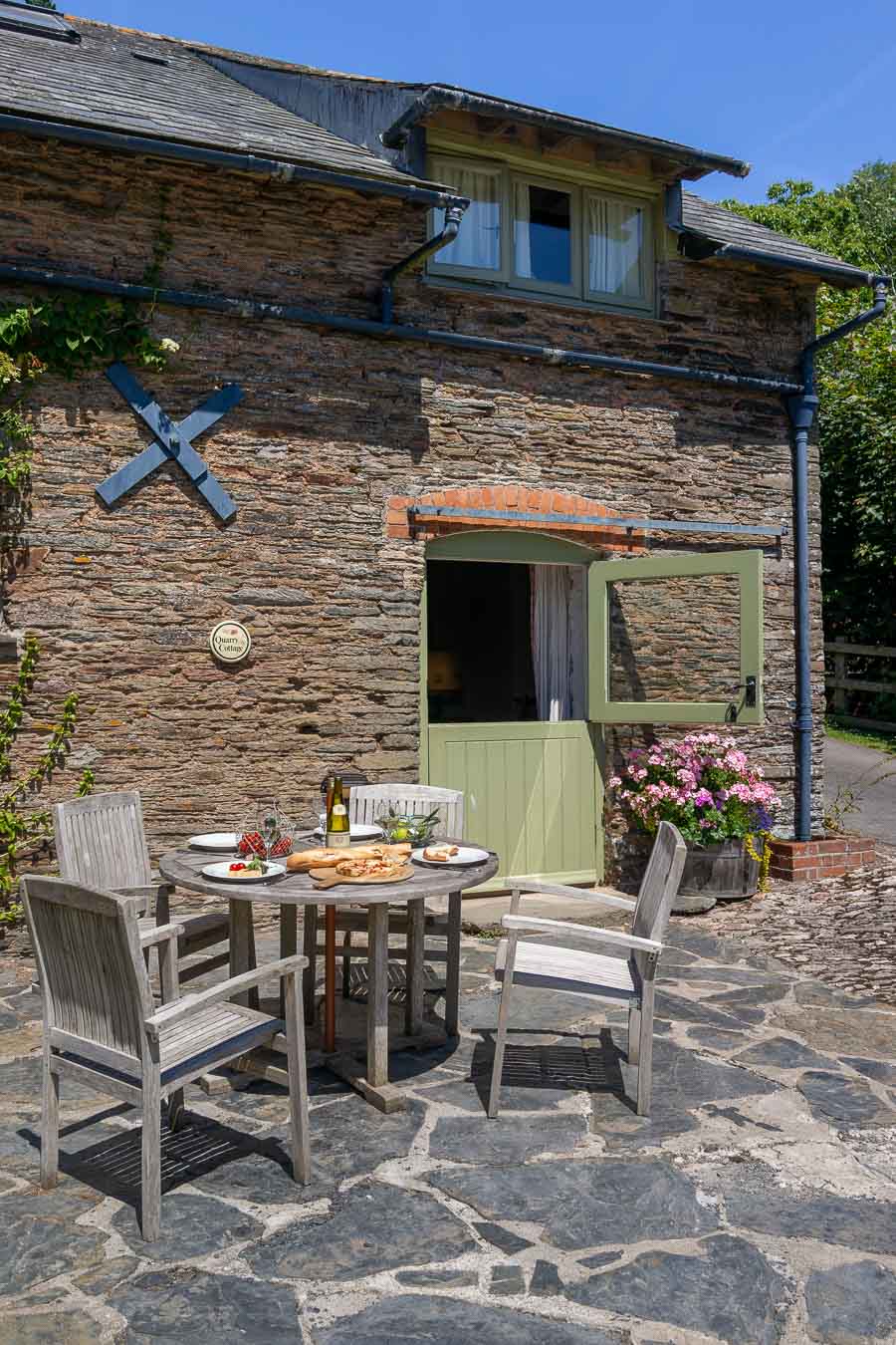 The stable door and original slate and stone of Quarry cottage Flear Farm. With wooden outdoor furniture for four and slate patio area looking onto the rolling green Devon hills. 