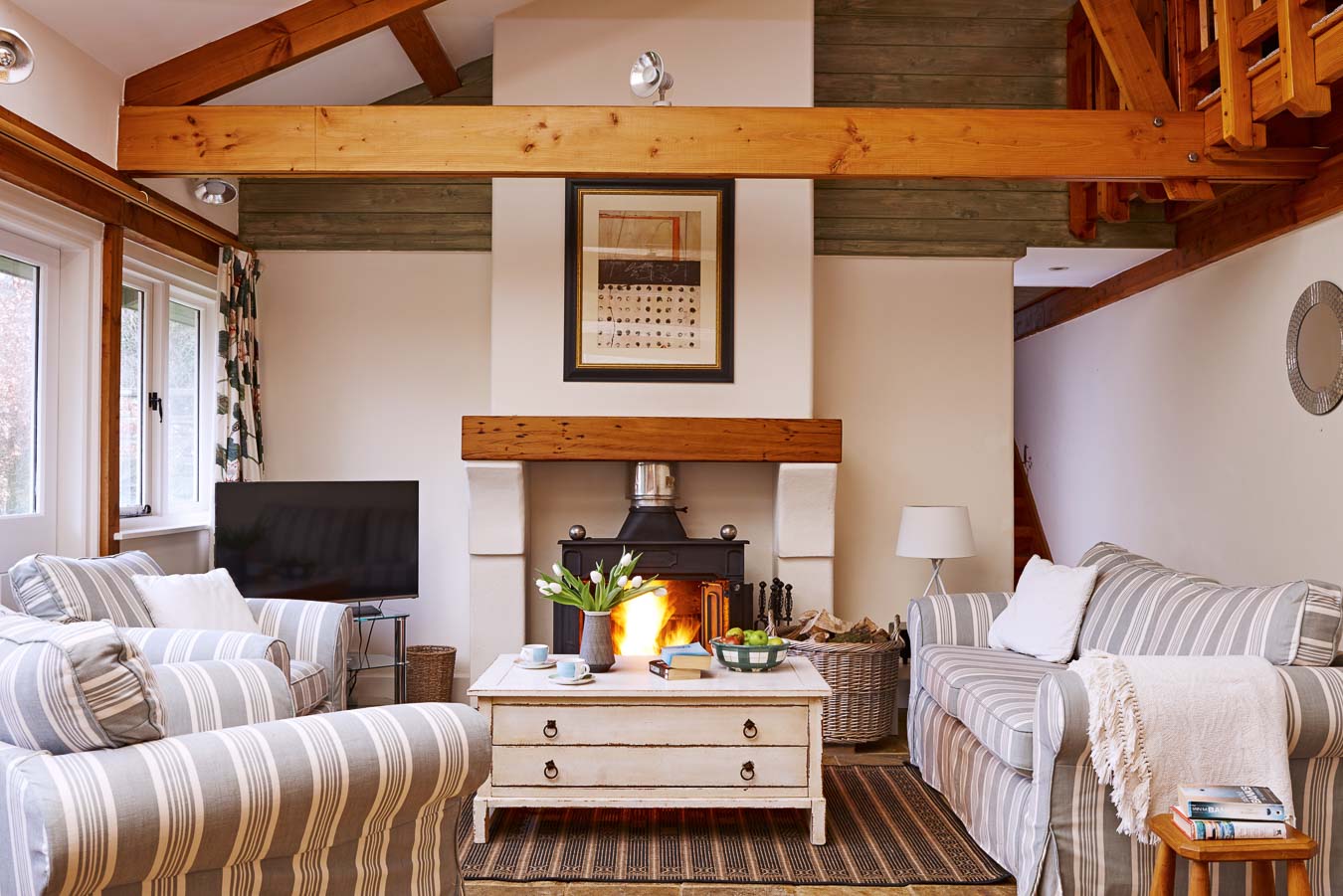 The open plan living room with exposed beams, flat screen TV and log burning stove at The Linhay cottage Flear Farm.