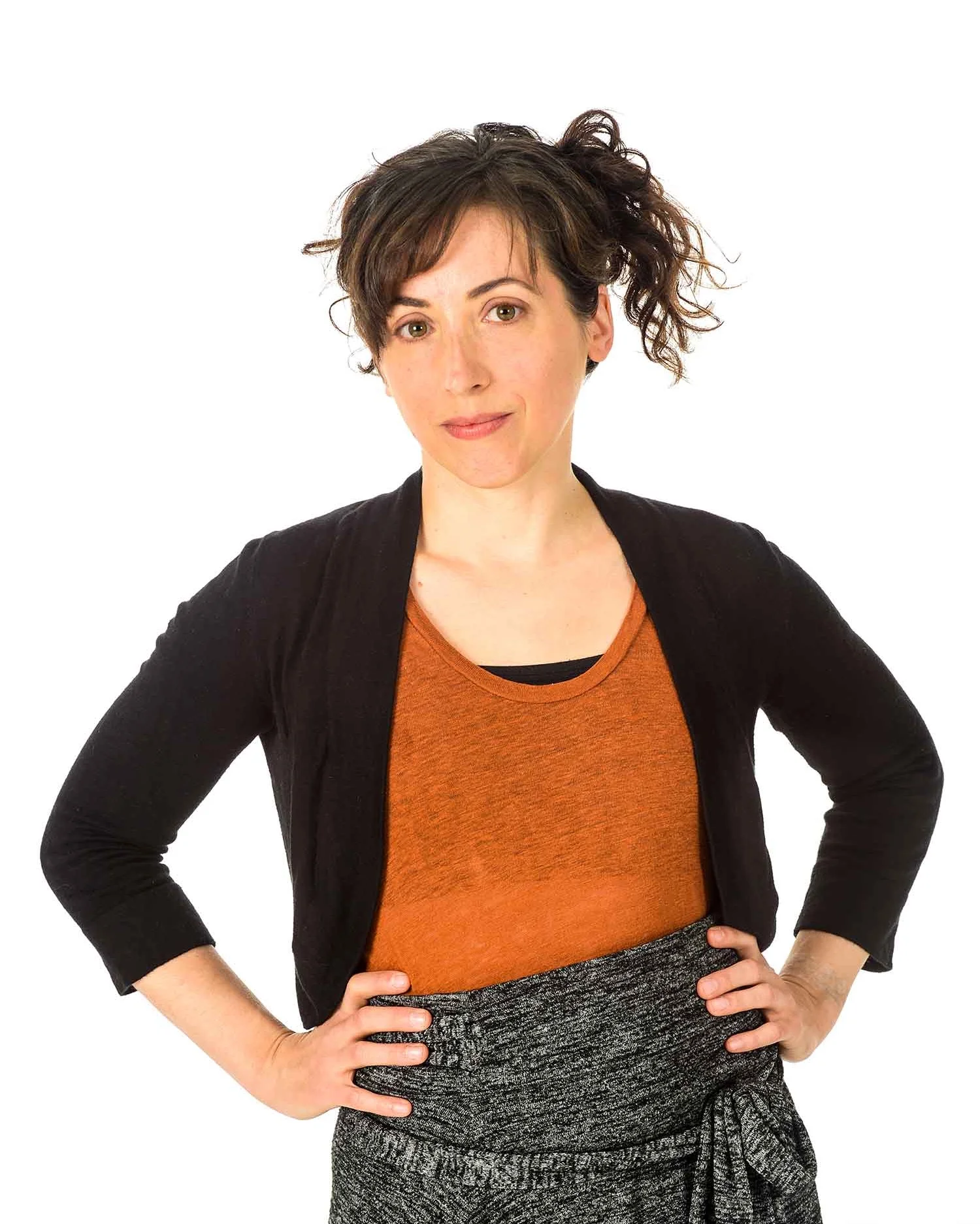 Amanda standing with hands on hips - hair is up, black sweater, rust top, grey skirt.