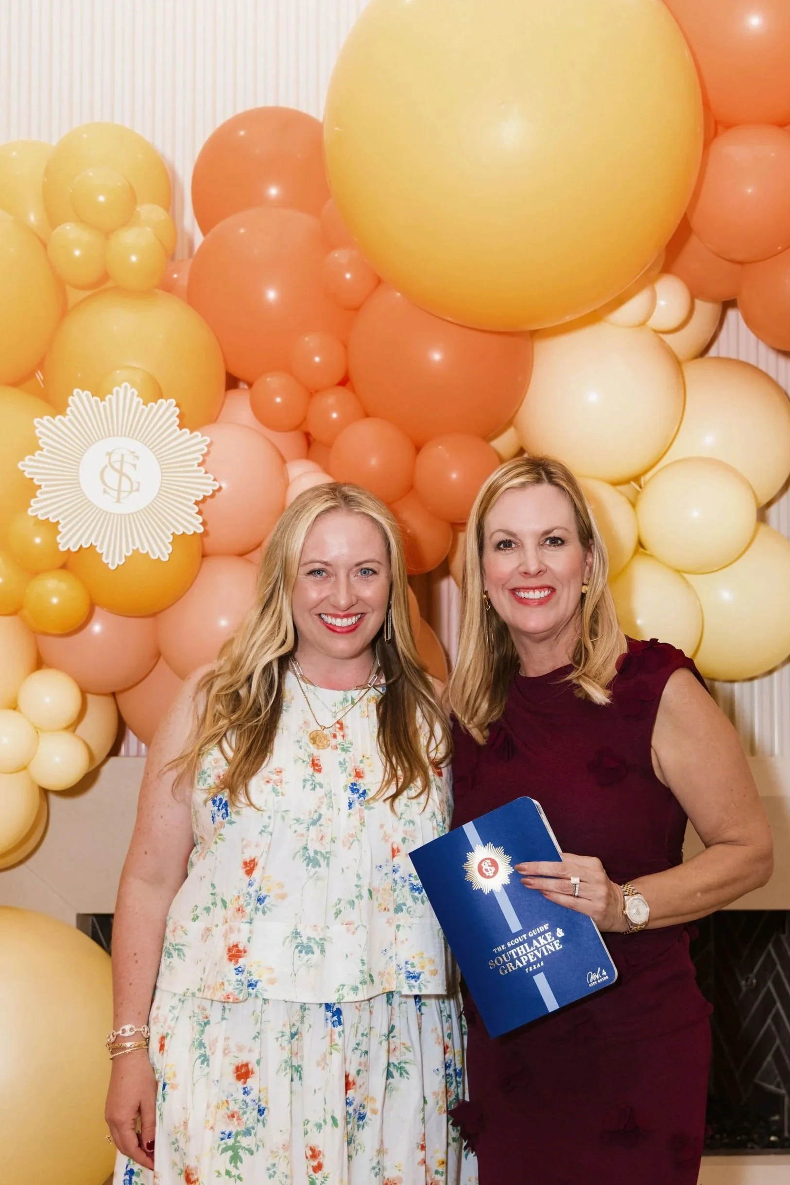 Two guests holding The Scout Guide Southlake & Grapevine in front of Up Up’s balloon backdrop.