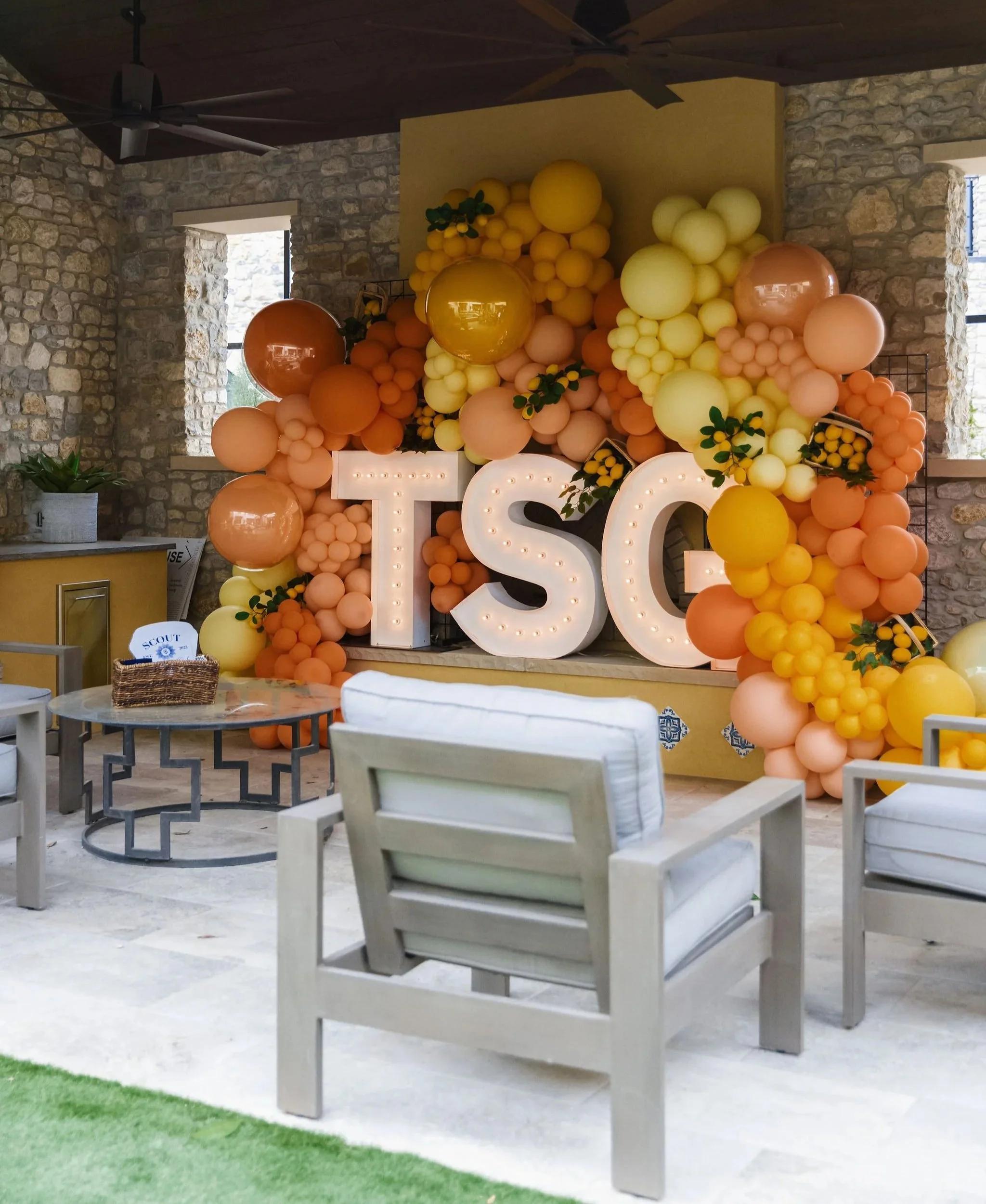 Up Up balloon backdrop with peach and yellow balloons, lemon accents, and illuminated TSG letters.