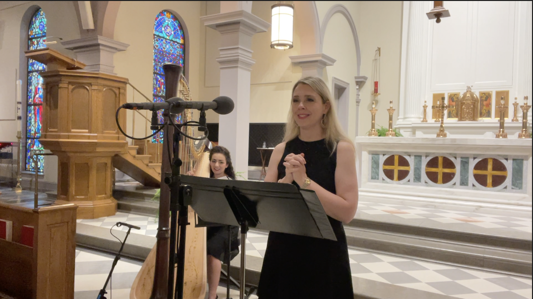 Carly York singing at a parish Mass with Christa Dalmazio playing harp in a large church