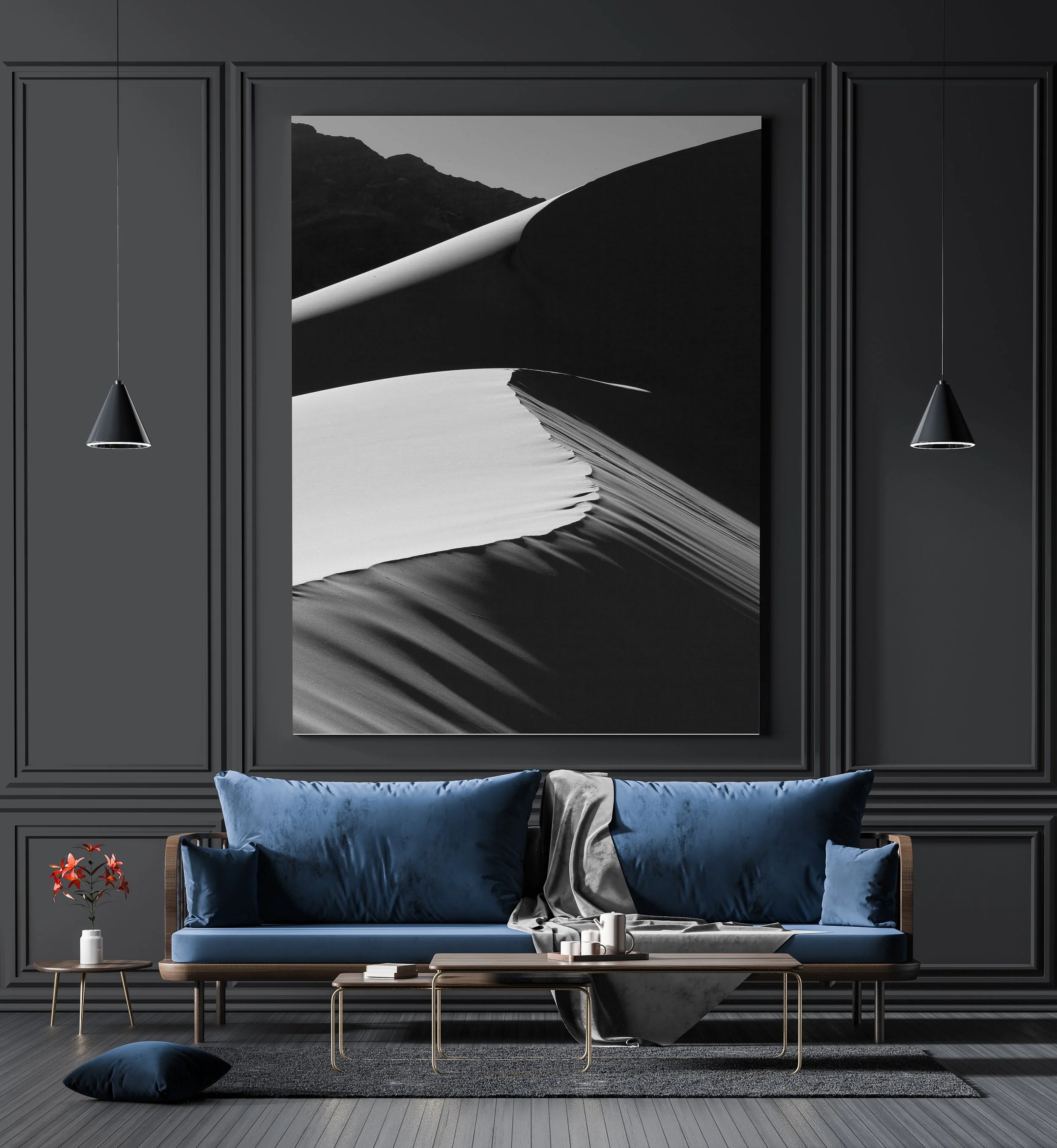 Modern living room with dark gray paneled walls, black and white abstract art, blue sofas, black rug, side table with red flowers, coffee table with candles, and minimalist lighting fixtures.
