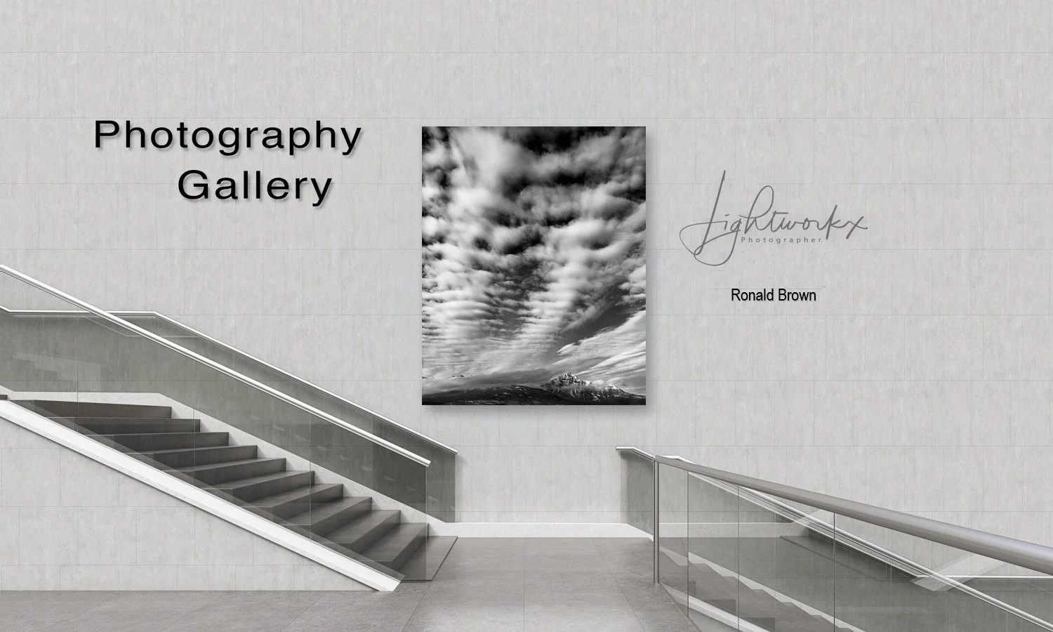 Black and white photograph of cloud-filled sky with mountains in the background displayed in a gallery setting.
