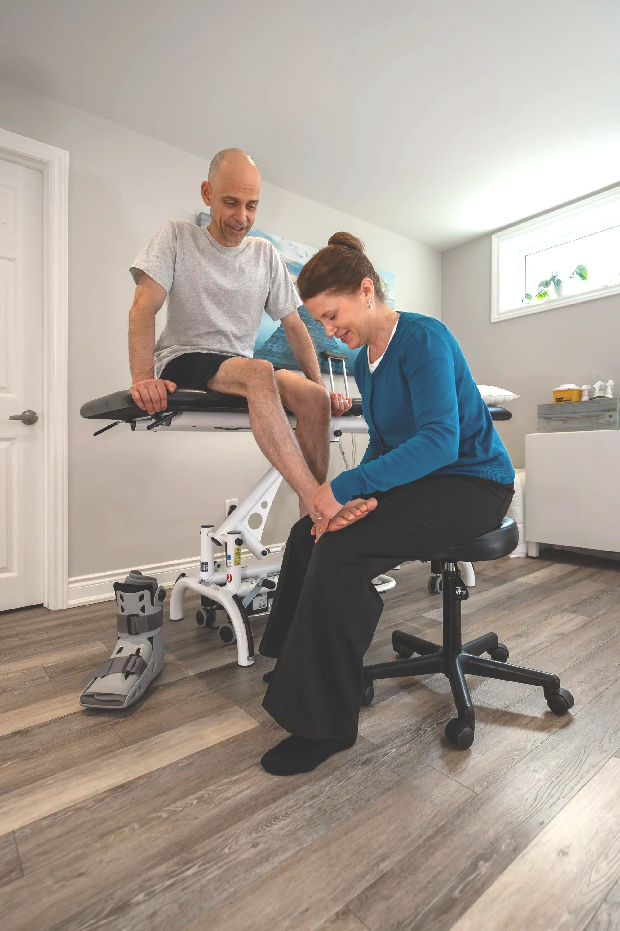 Physical therapist assisting a man with a leg injury during rehabilitation exercise in a clinic room.