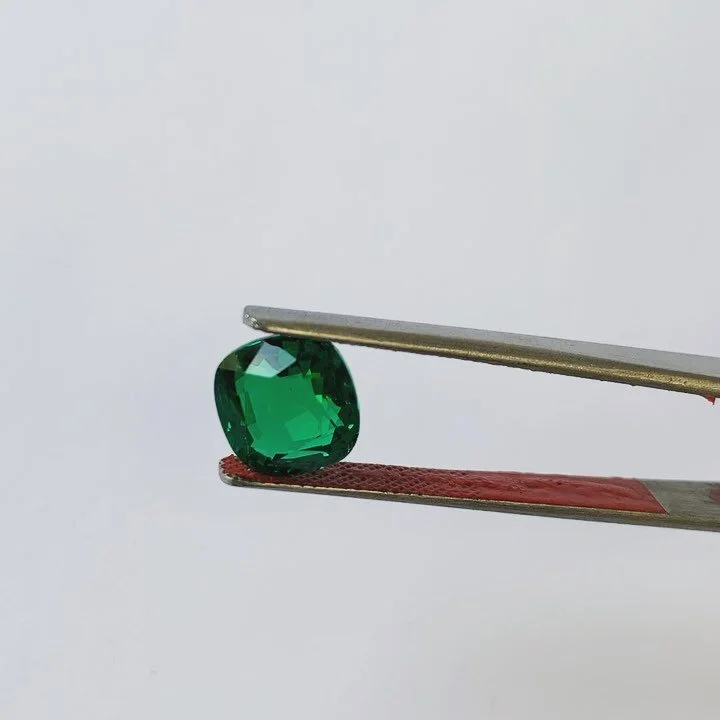A green gemstone held in tweezers