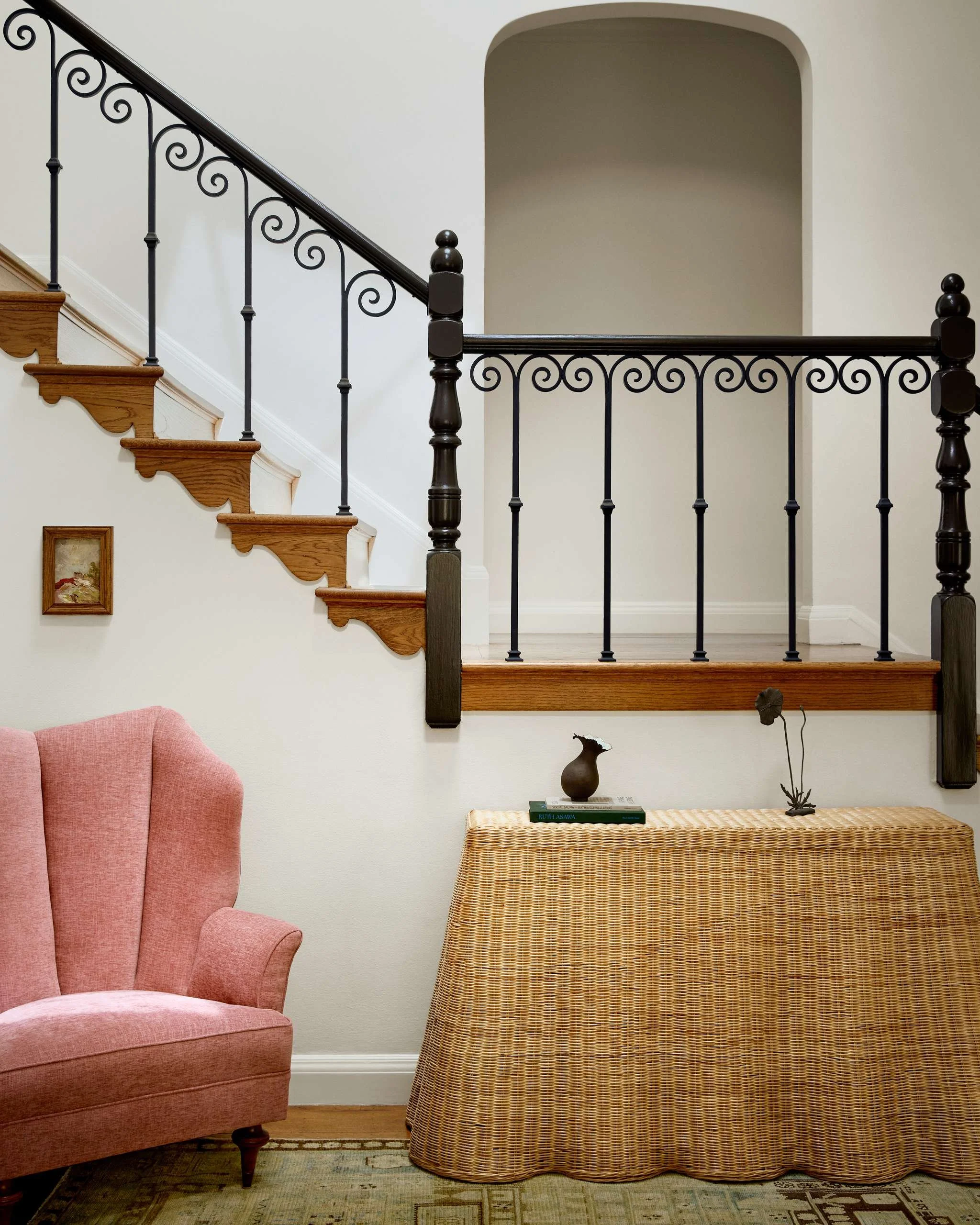 1940s Arturo Pani wingback chair and scalloped wicker console beneath a scrolled wrought-iron stair railing