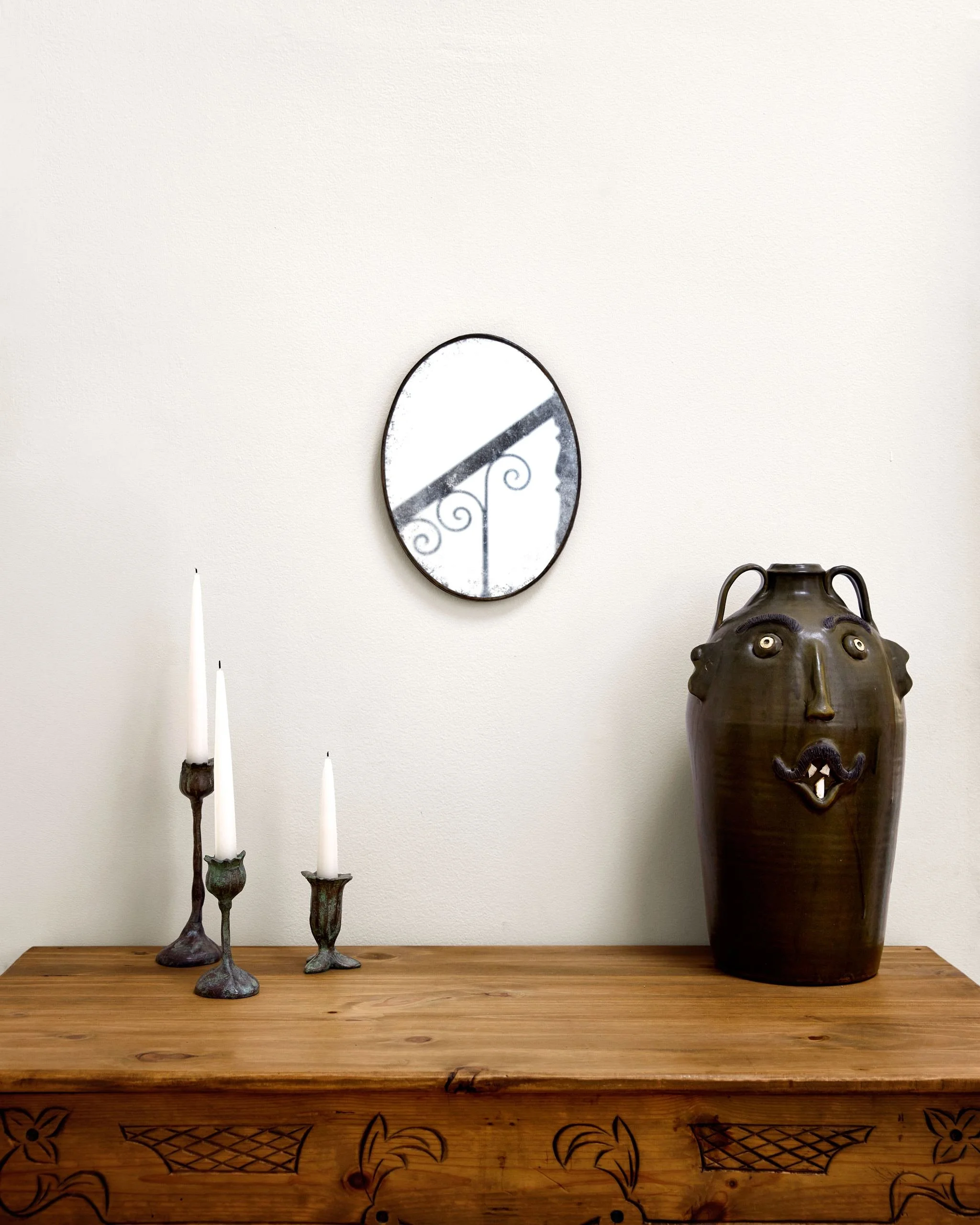 Carved antique Spanish pine dresser with ceramic face jug, bronze candlesticks and an oval mirror reflecting the iron stair
