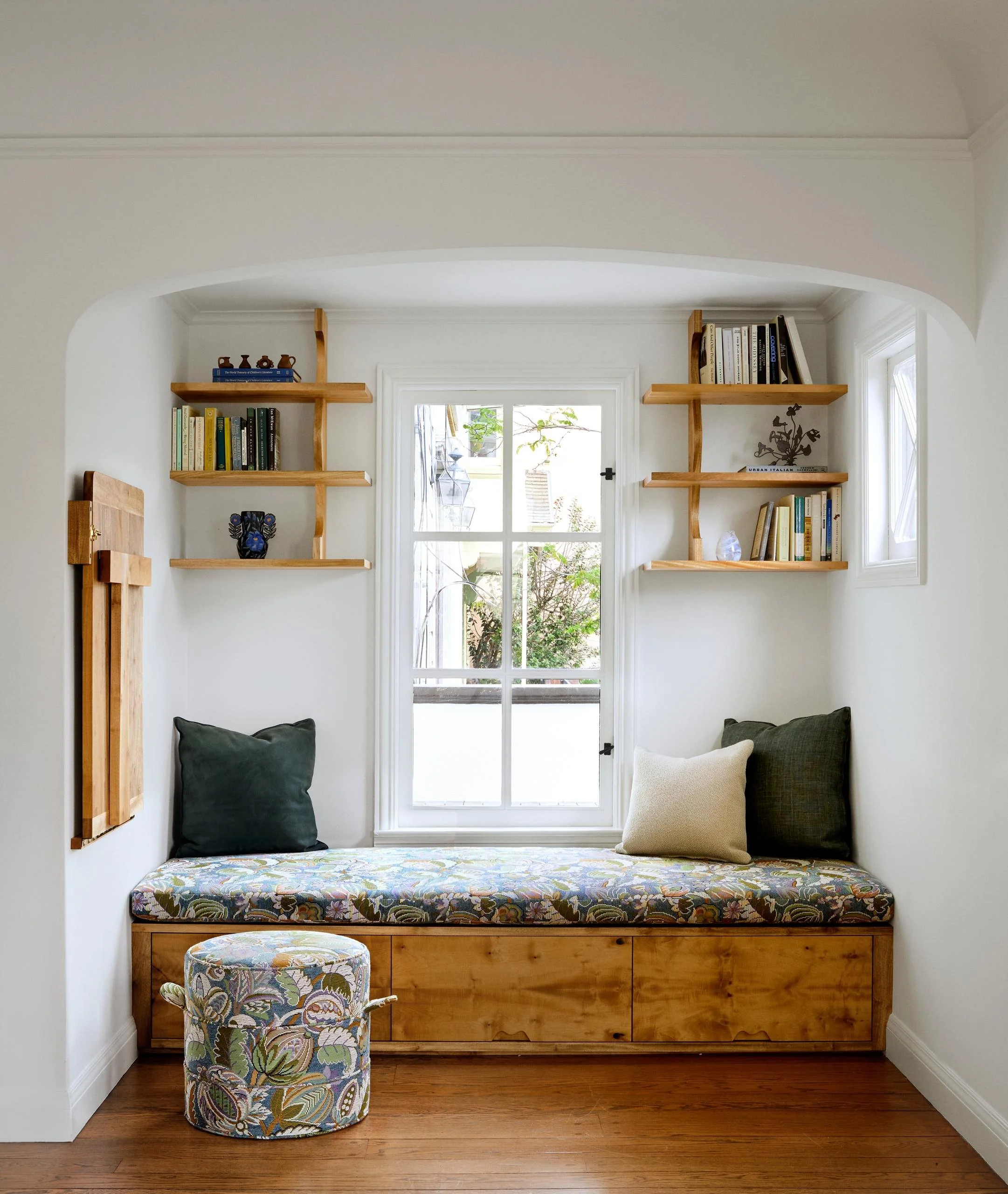 Reading nook with the desk folded flat, wood storage bench in botanical fabric and a matching round ottoman