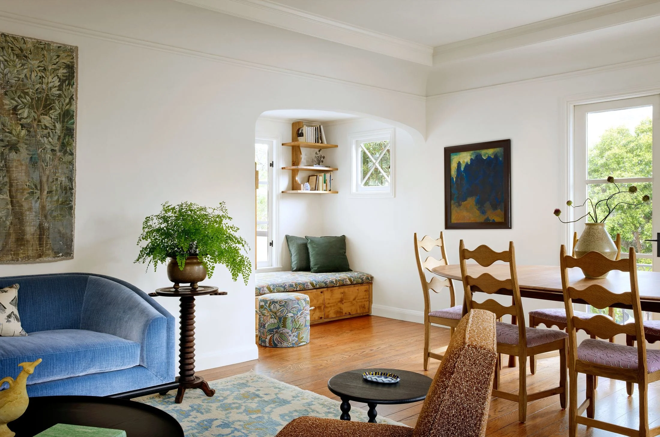 Living and dining room with Nickey Kehoe blue velvet sofa, original plaster archway to a reading nook, and wavy ladder-back dining chairs