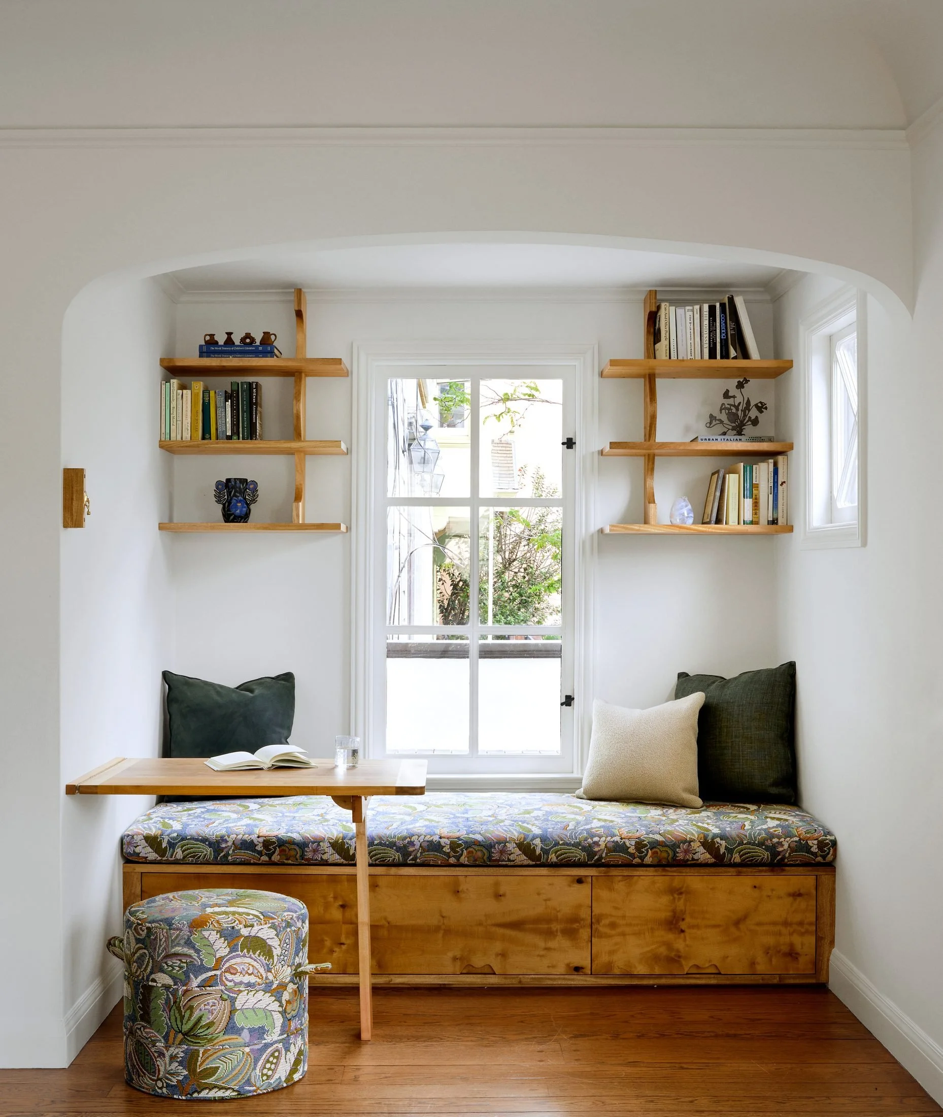 Custom reading nook in an arched alcove, with botanical-fabric window bench, open shelves and a fold-down desk