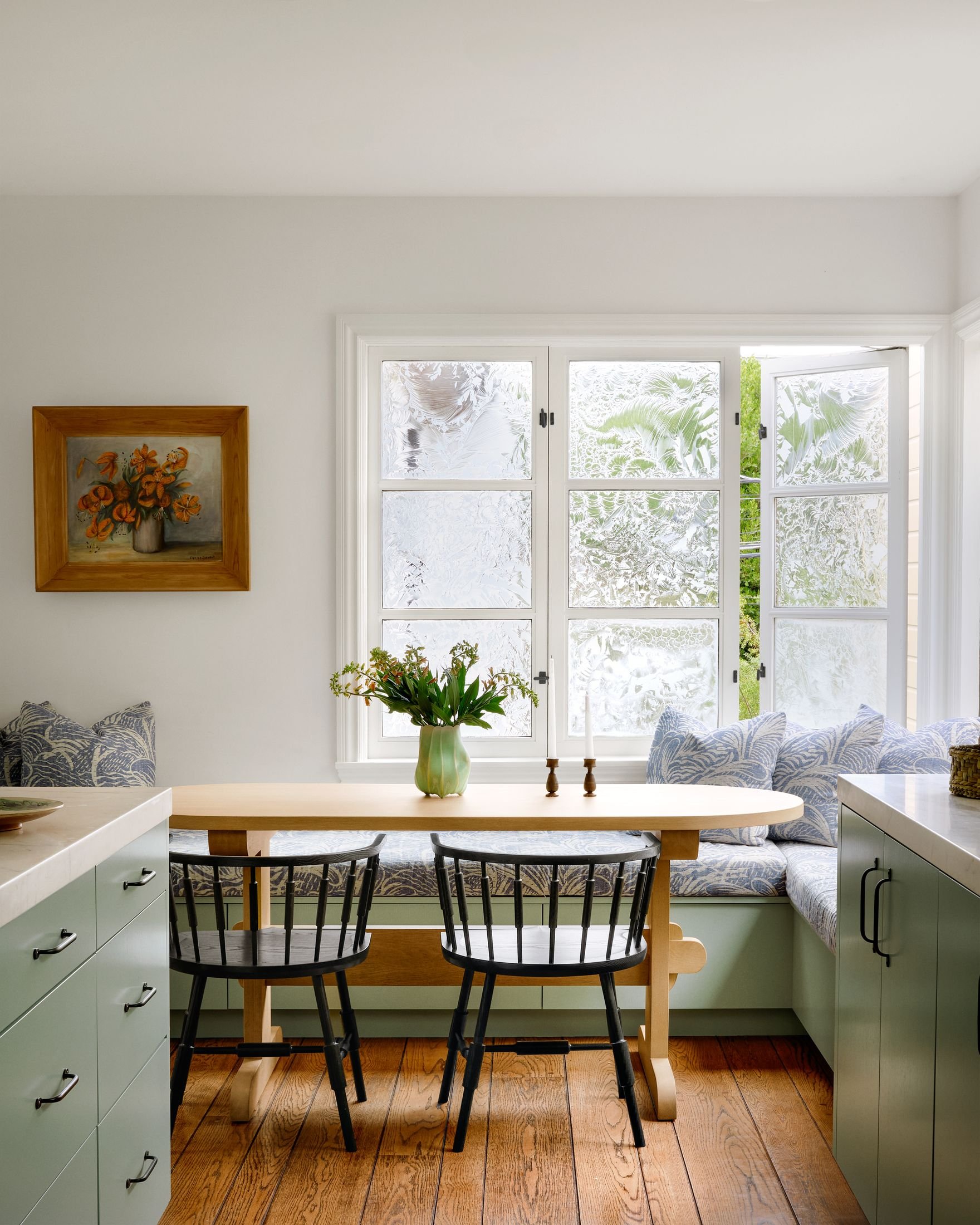 Kitchen breakfast banquette with sage green cabinetry, oak trestle table, black spindle chairs and textured glass windows