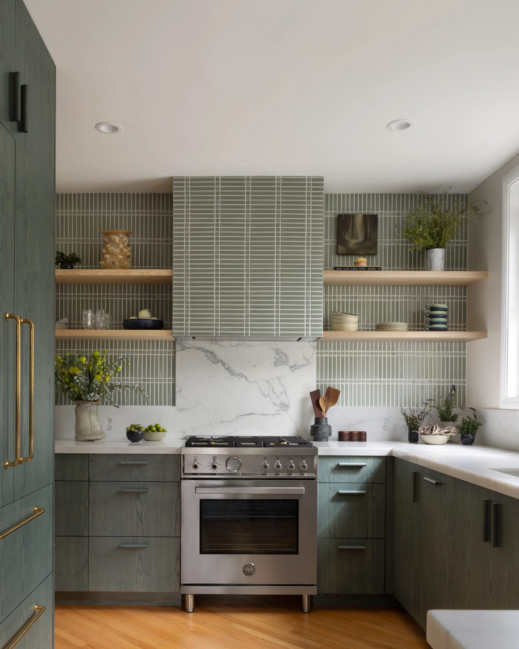Kitchen with green-stained ash cabinetry, handmade green tile range hood, oak shelves and marble backsplash