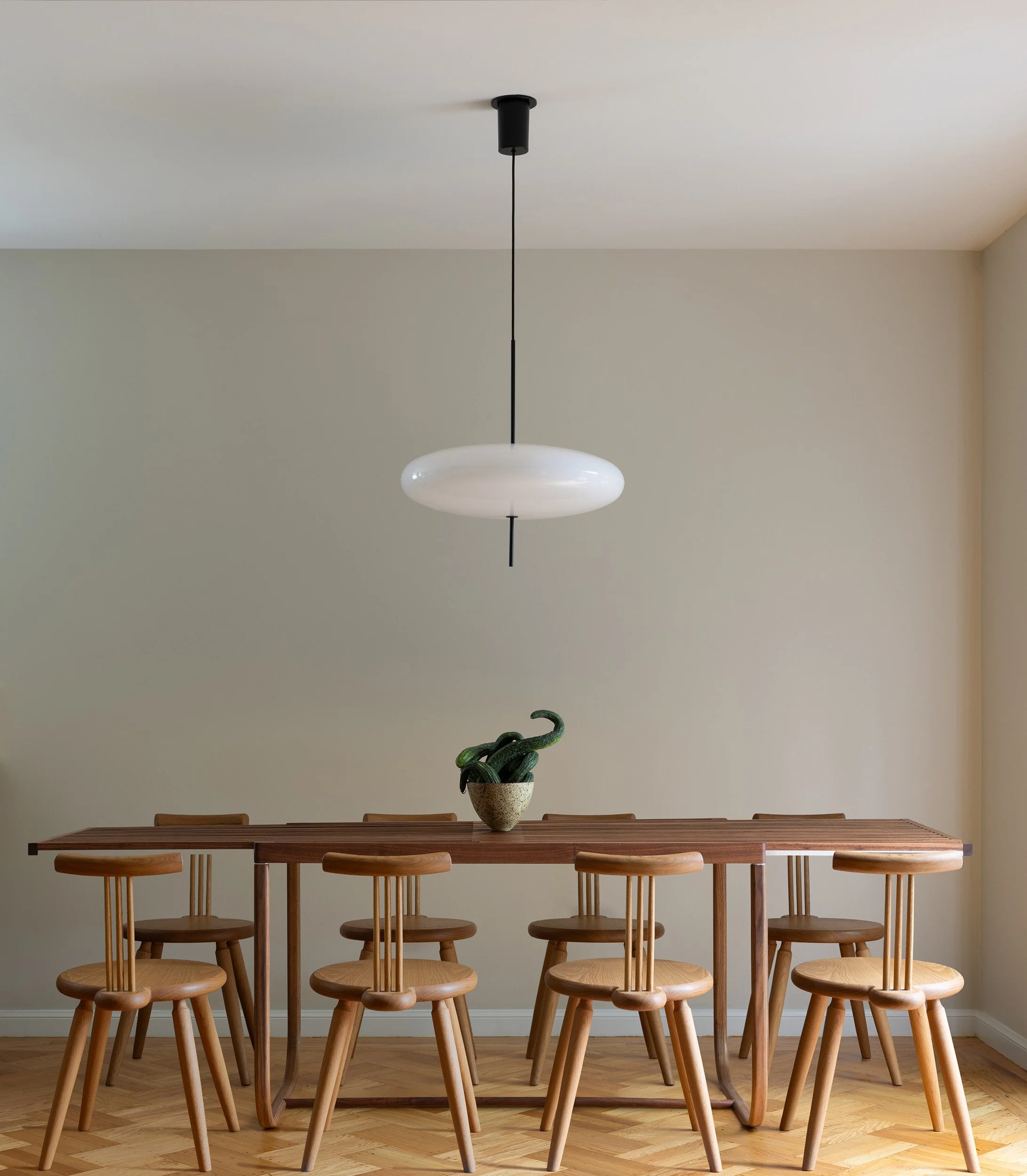 Custom expandable wood dining table with carved wood stools under a white disc pendant light, San Francisco