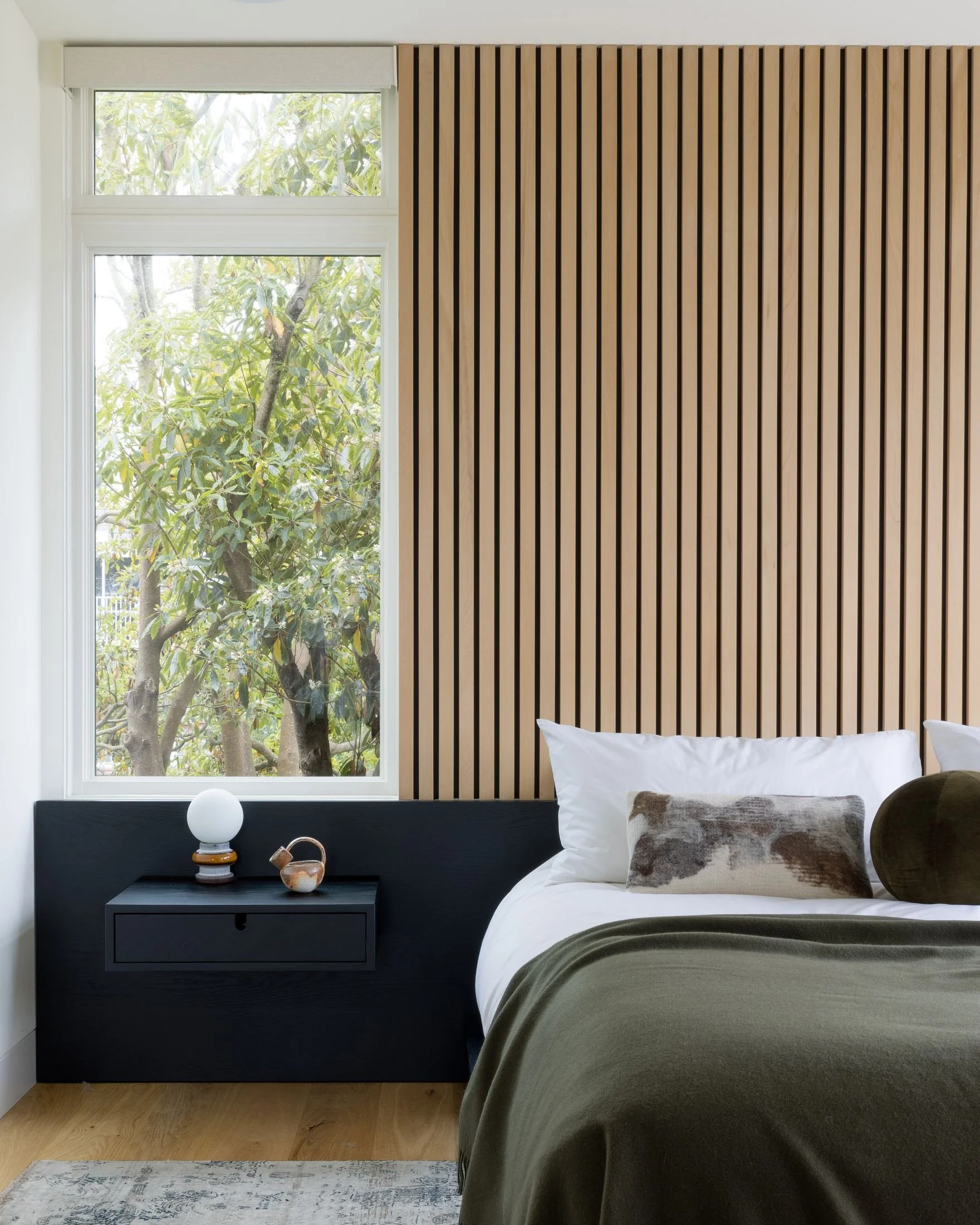 Bedroom with floor-to-ceiling slatted wood headboard wall, navy floating nightstand and olive bedding, Cole Valley
