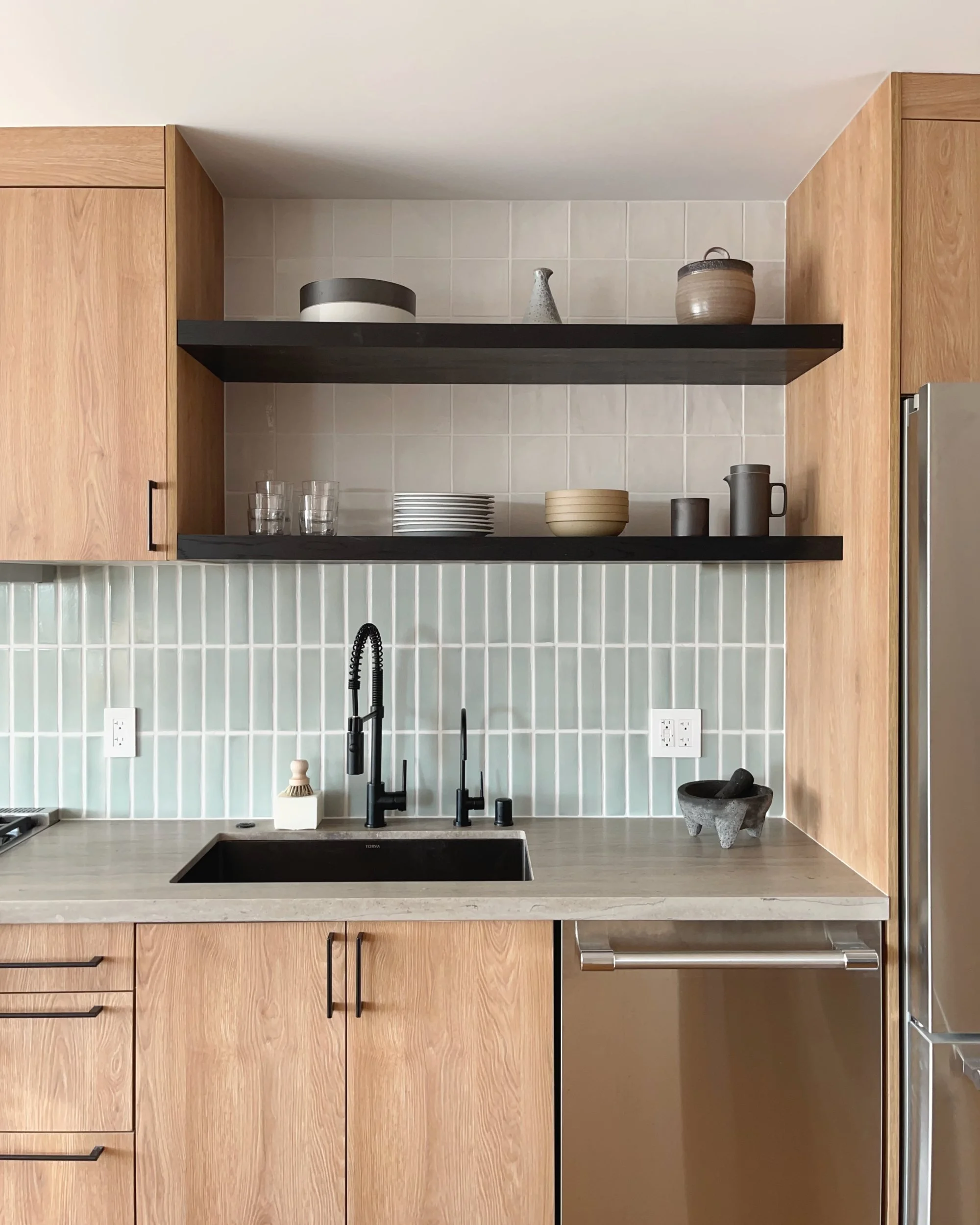 Kitchen near Ocean Beach with wood cabinetry, sage green vertical tile, black open shelves and black faucet