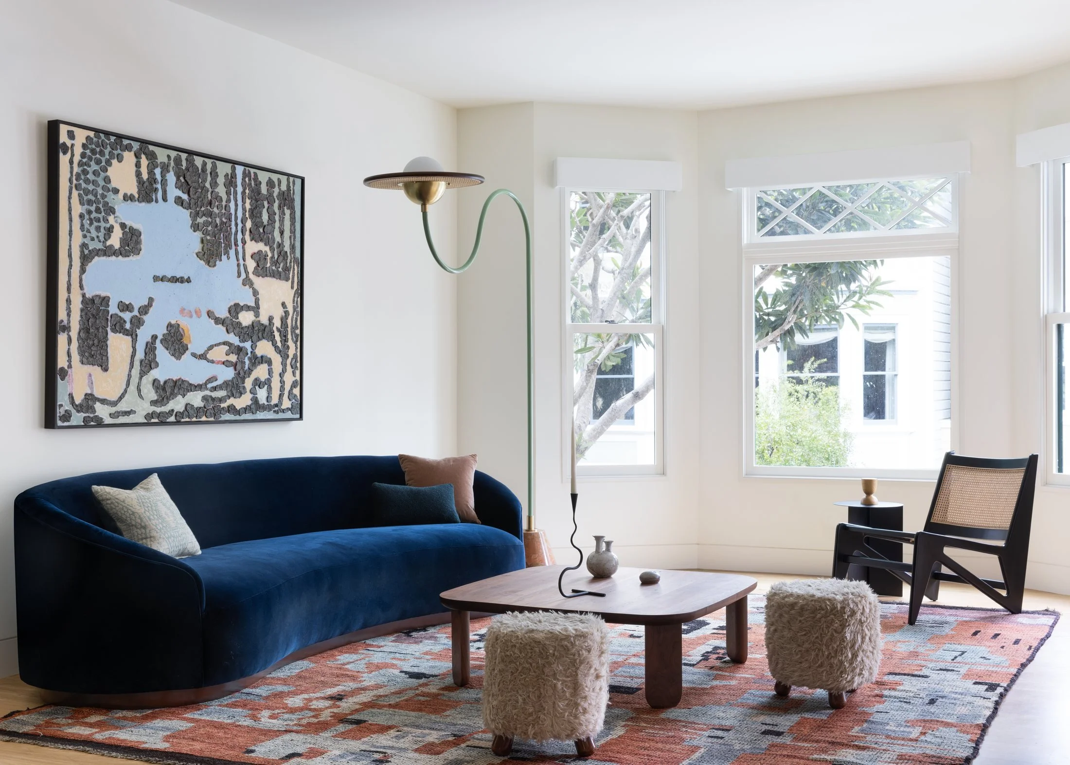 Edwardian front parlor with bay windows, curved navy velvet sofa, shearling stools and red wool rug, Cole Valley