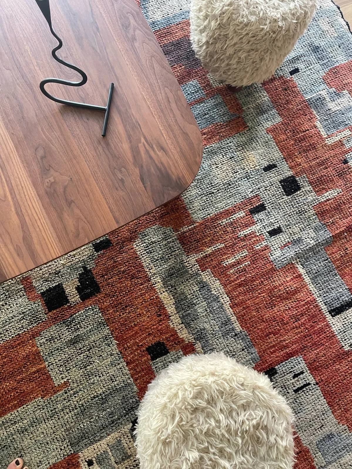 Detail of shearling stools and a walnut coffee table on a handwoven terracotta and blue rug in the front parlor