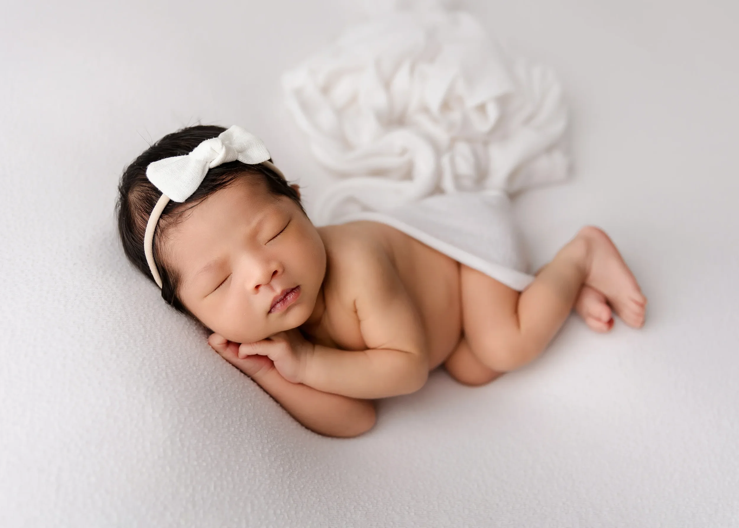 Newborn baby sleeping and wearing a white bow, by San Francisco Photographer Eva Baker
